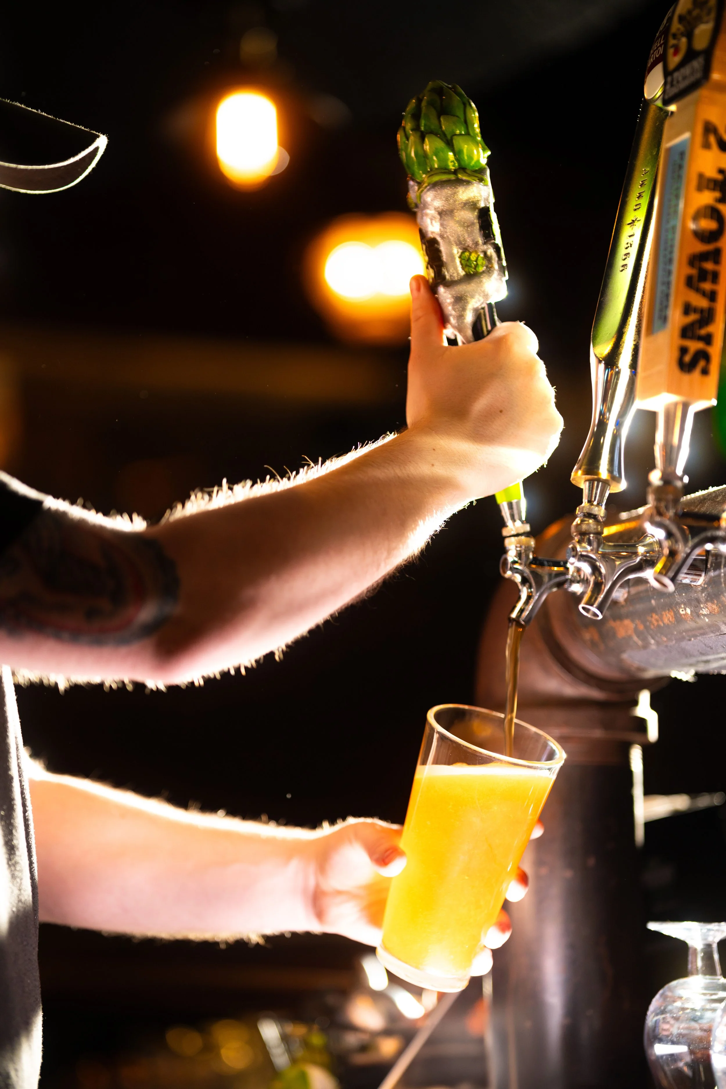Person pouring draft beer into a pint glass at a bar