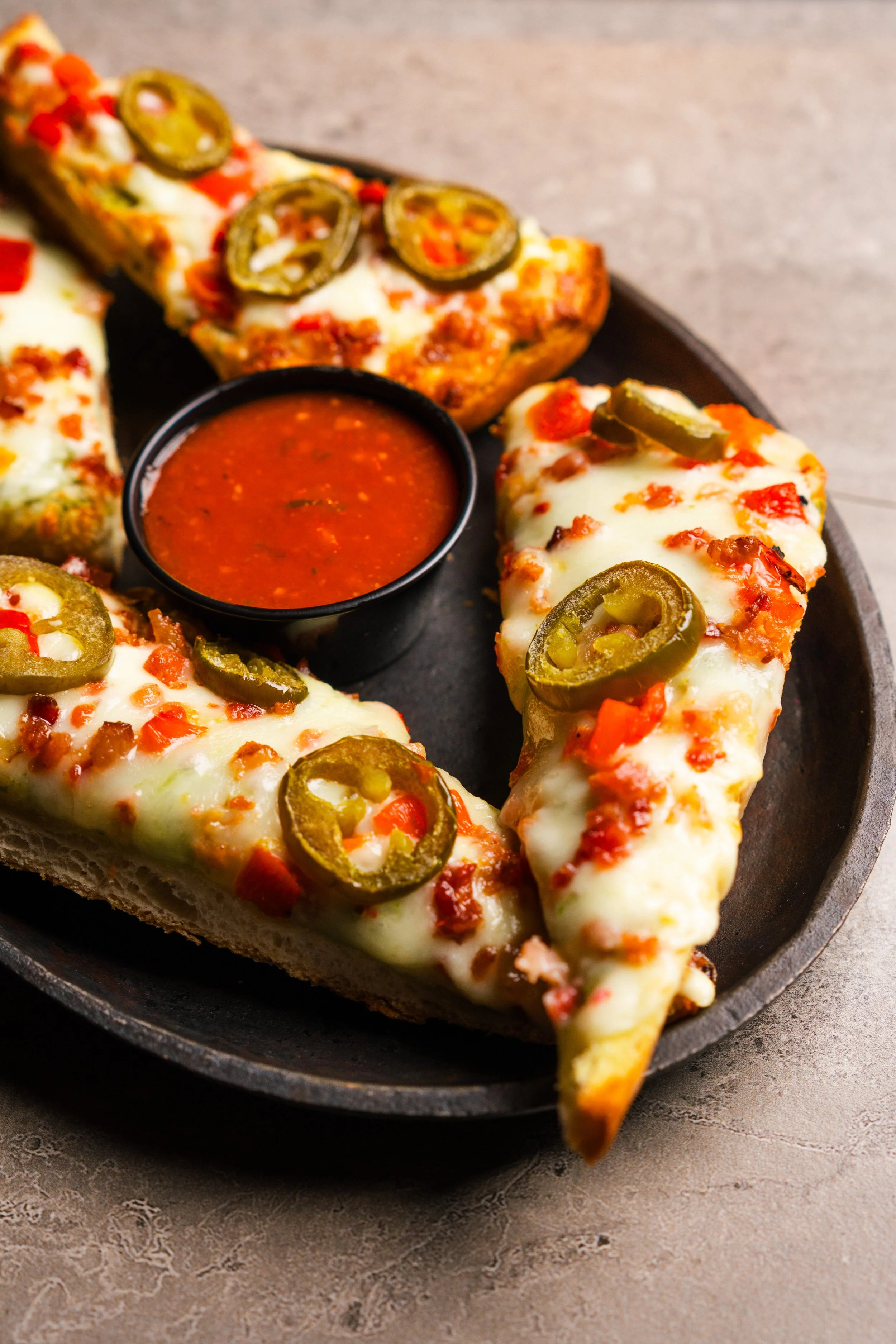 Slices of cheesy jalapeño bread with marinara sauce in a black dish.