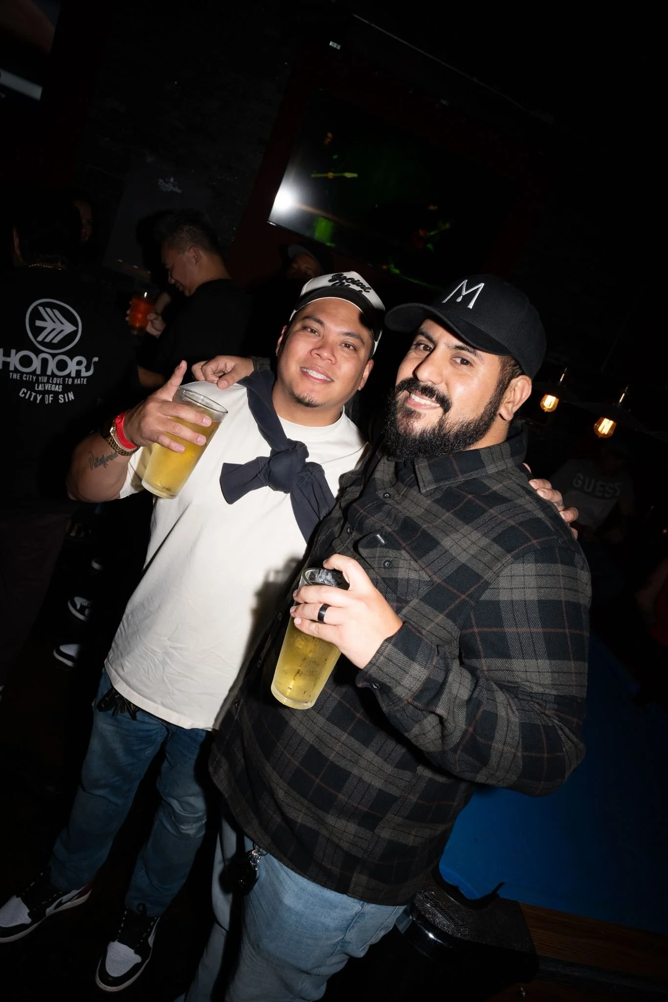 Two men smiling and holding drinks in a bar or nightclub.