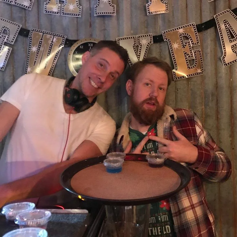 Two men at a New Year's party with drinks and decorations.