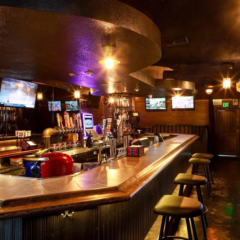 Interior of a bar with a long counter, bar stools, draft beer taps, and multiple television screens.