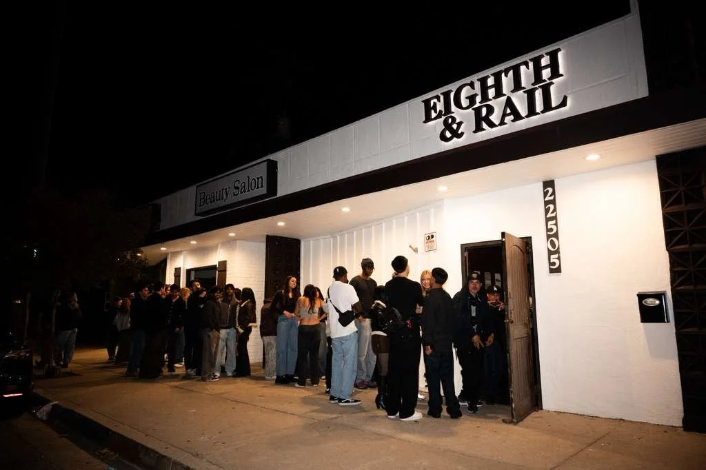 Line of people waiting outside a business called Eighth & Rail at night.