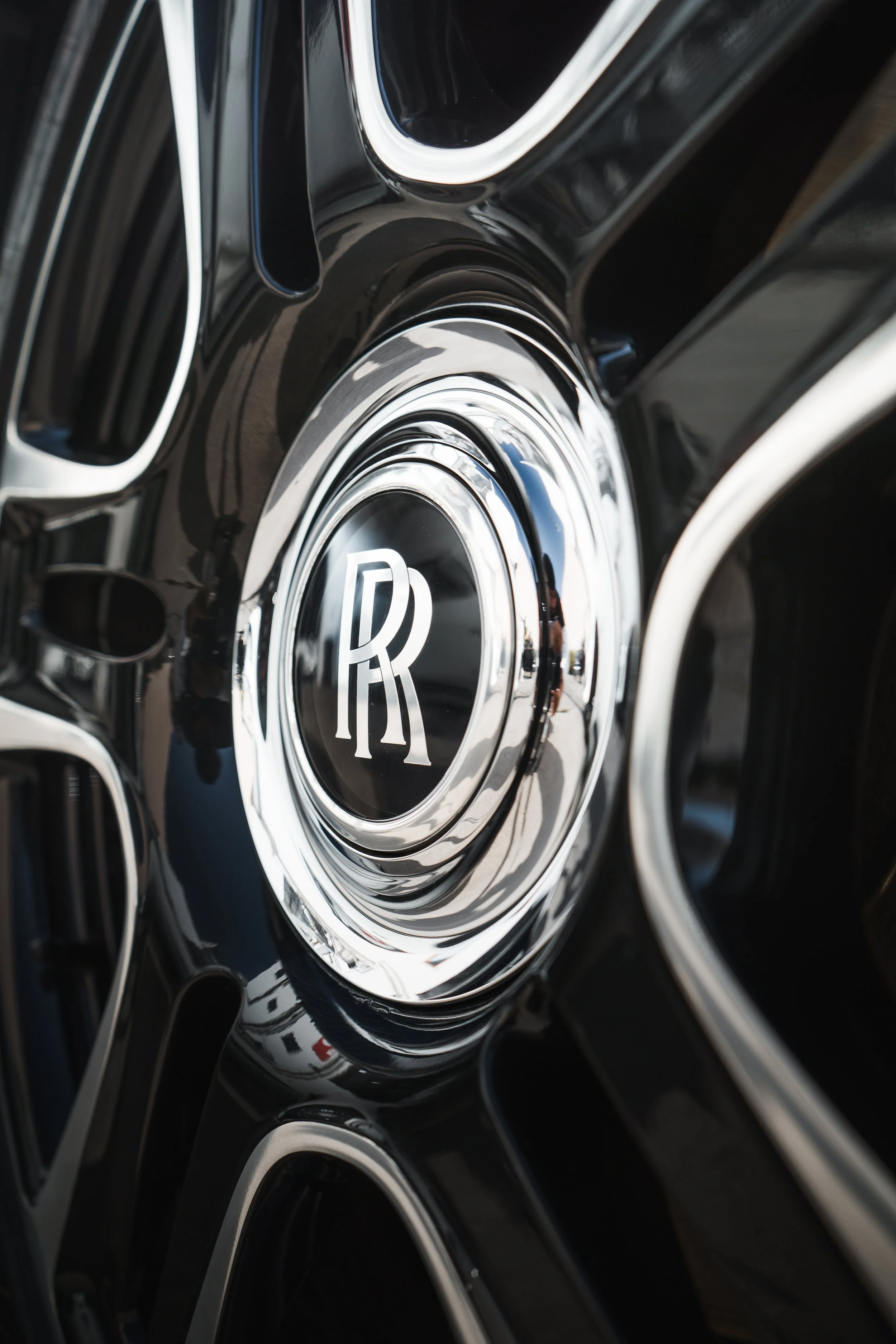 Close-up of a black and chrome Rolls-Royce wheel with a prominent Rolls-Royce emblem in the center.