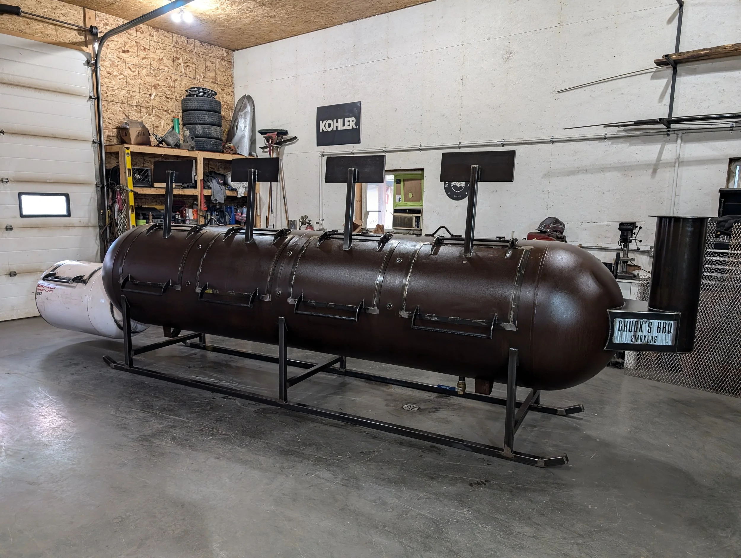 Large smoker grill in a garage with the label "Chuck's BBQ."