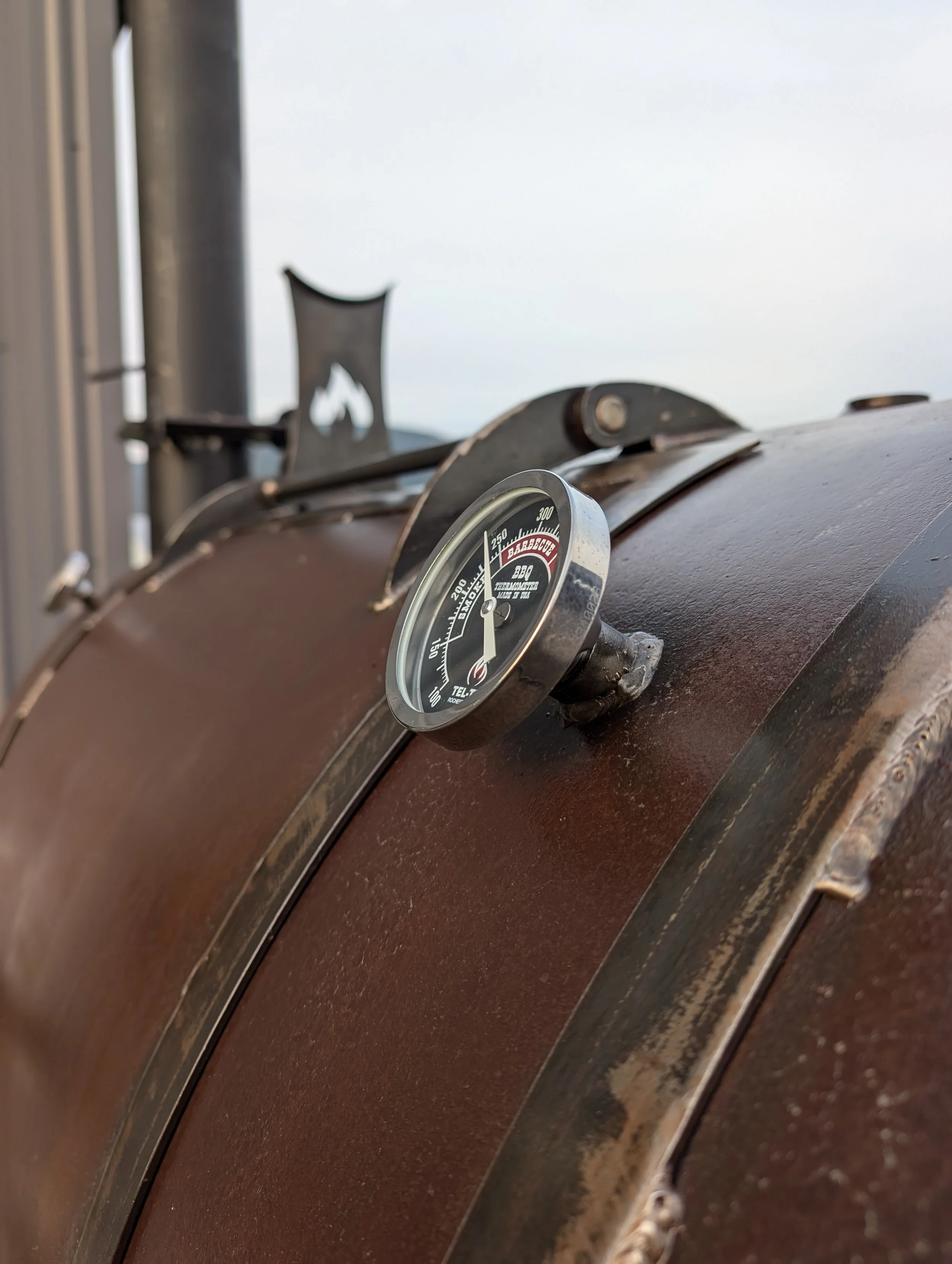 Close-up of a portable smoker with a temperature gauge attached, showing a temperature just below 250°F.