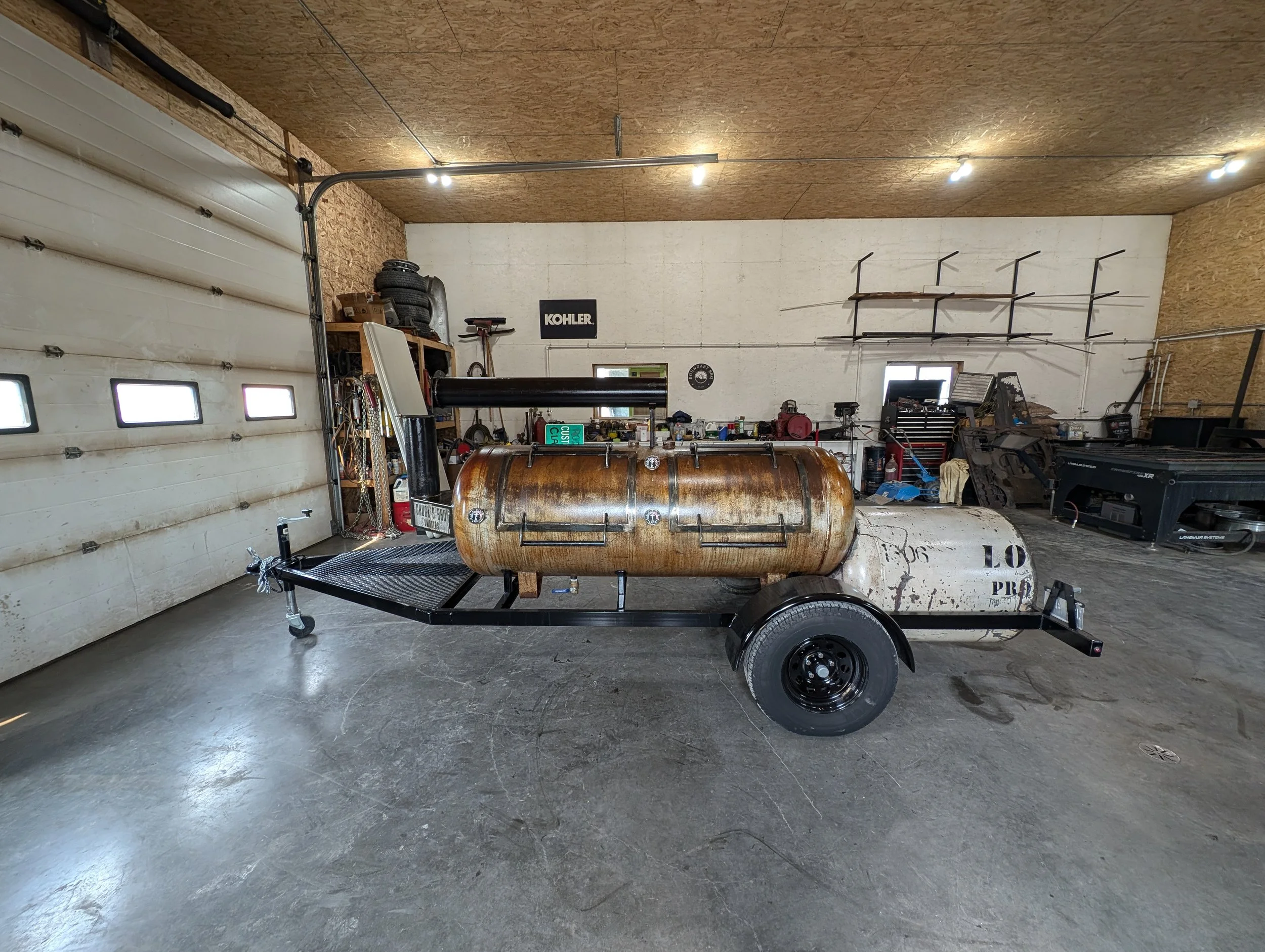 A trailer with an old propane tank mounted on it, parked inside a garage workshop.