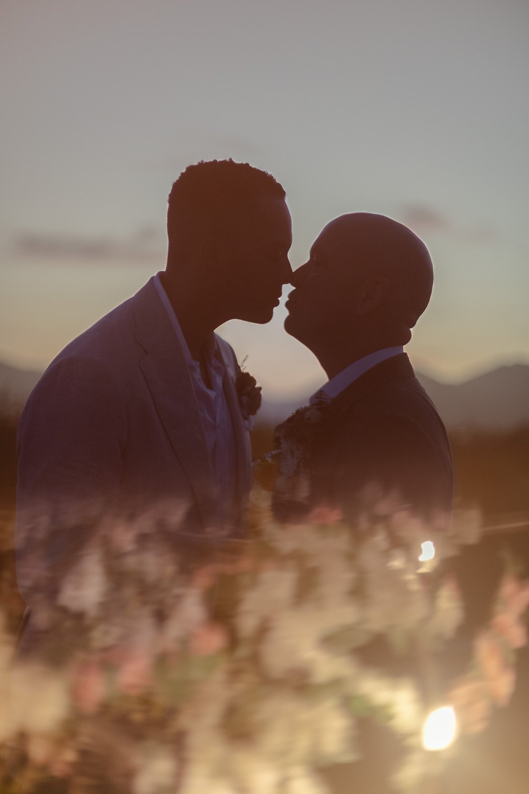 Two grooms silhouetted at sunset with floral reflections during their intimate destination wedding in Cabo, photographed by an LA wedding photographer.