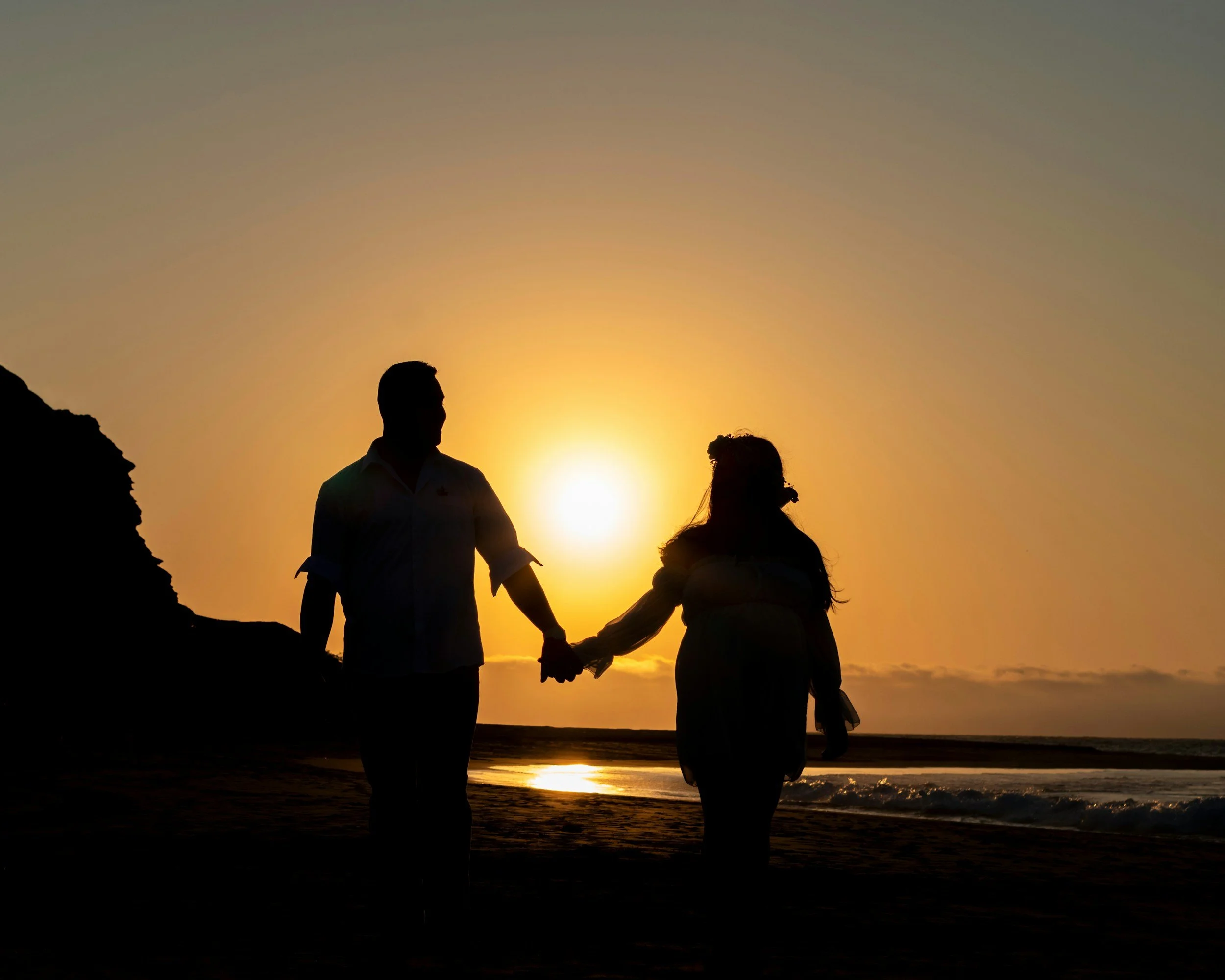 Woman and man holding hands on a beach, sunset