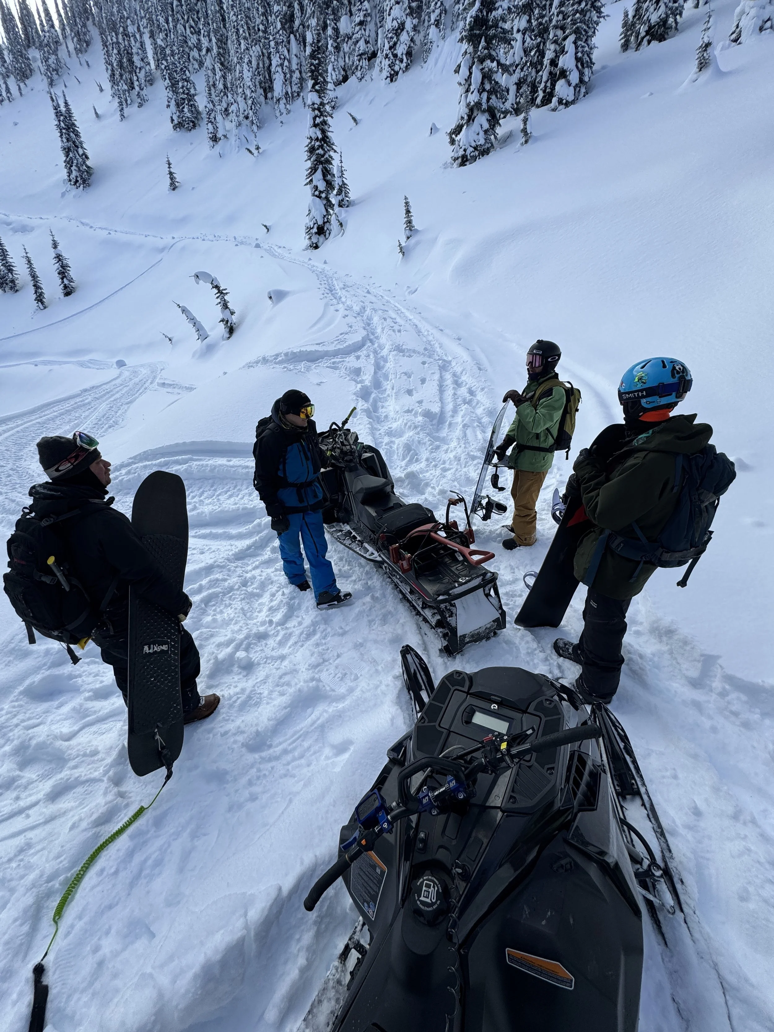 Group of four back country sledders, deciding how far up they should hike before they send it down the hill near Sandon, BC. 