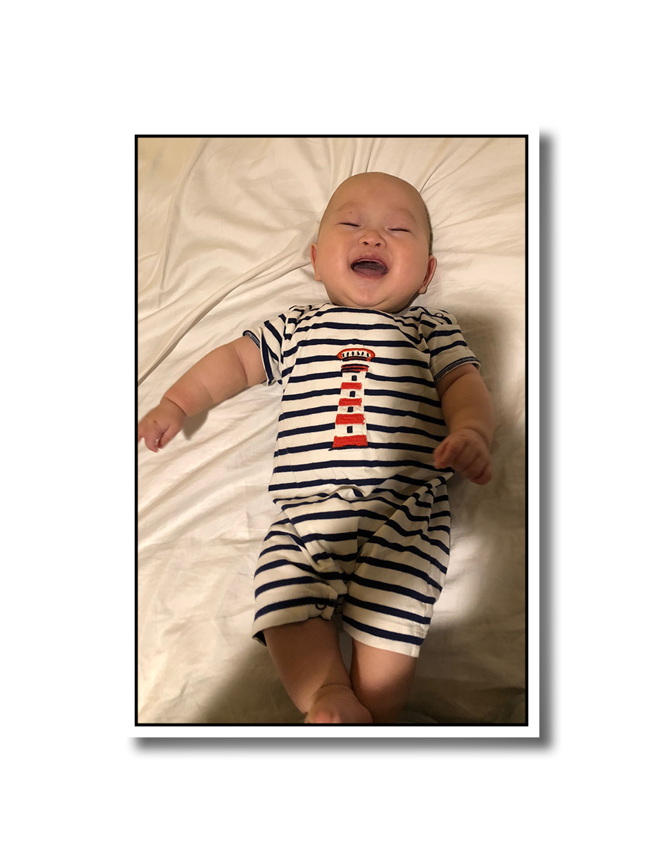 Baby Noah laying down on a bed, and giving a big toothless grin to the camera.