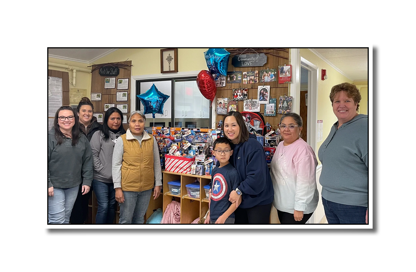 Photo of Grace, Kyle, and teachers from the community with a spread of kids care package donations. There is a strong Captain America theme.