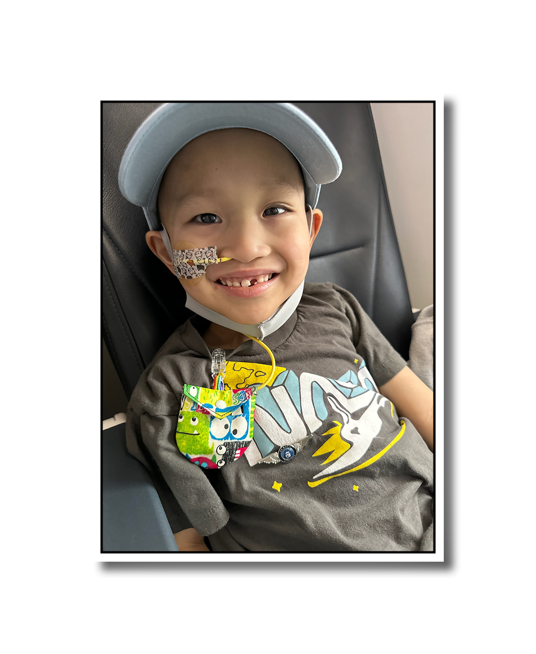 Noah smiling for the camera in an airplane seat. He wears a light blue hat and a tube in his nose.