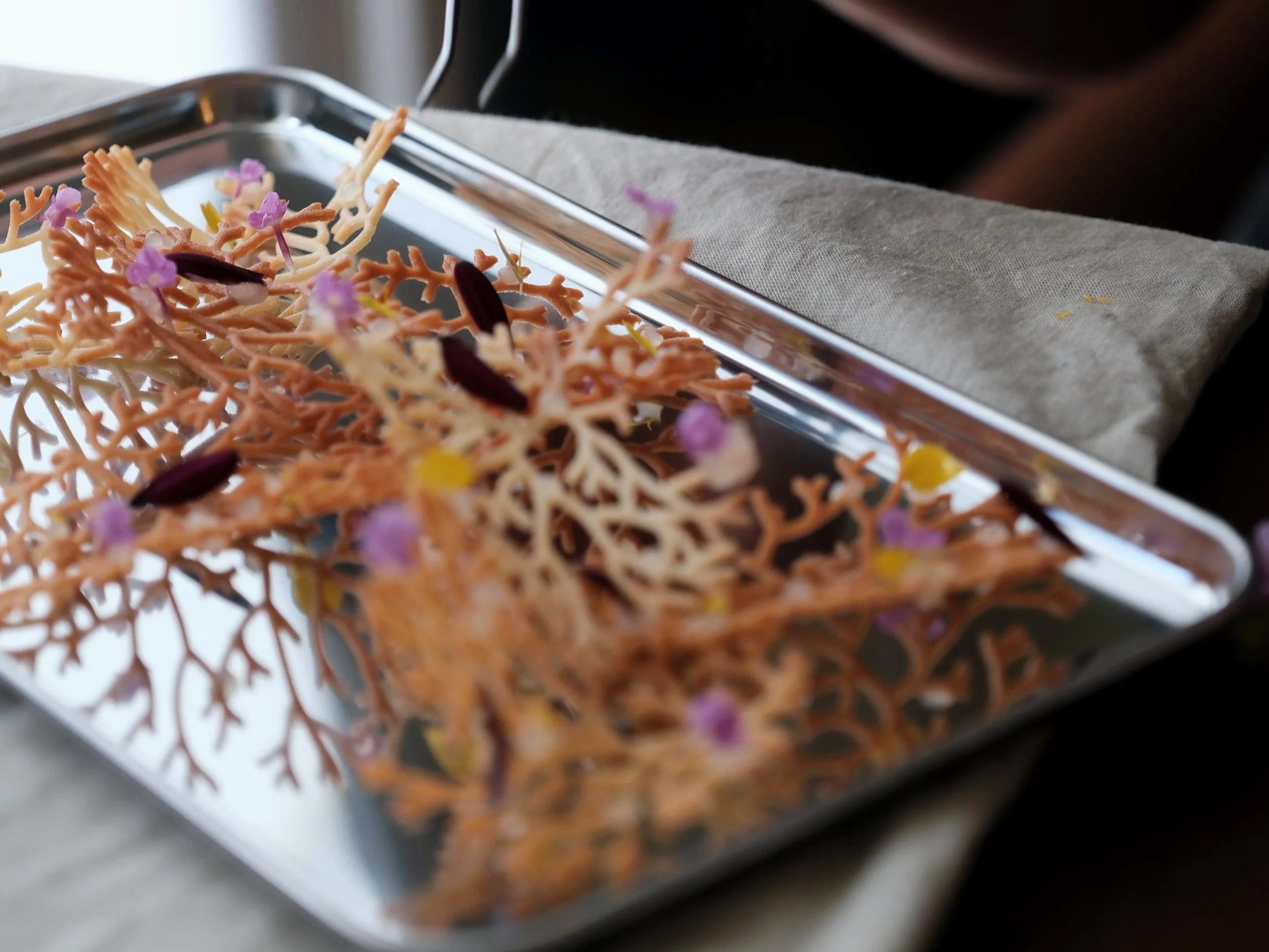 Decorative edible coral shape with small purple and yellow flowers on a silver tray.