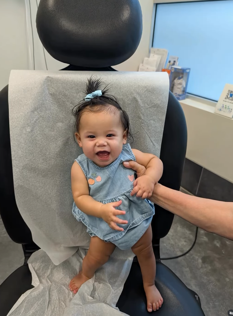A smiling baby standing in the dental exam chair at Kid-1 Pediatric Dentistry, held gently by a caregiver.