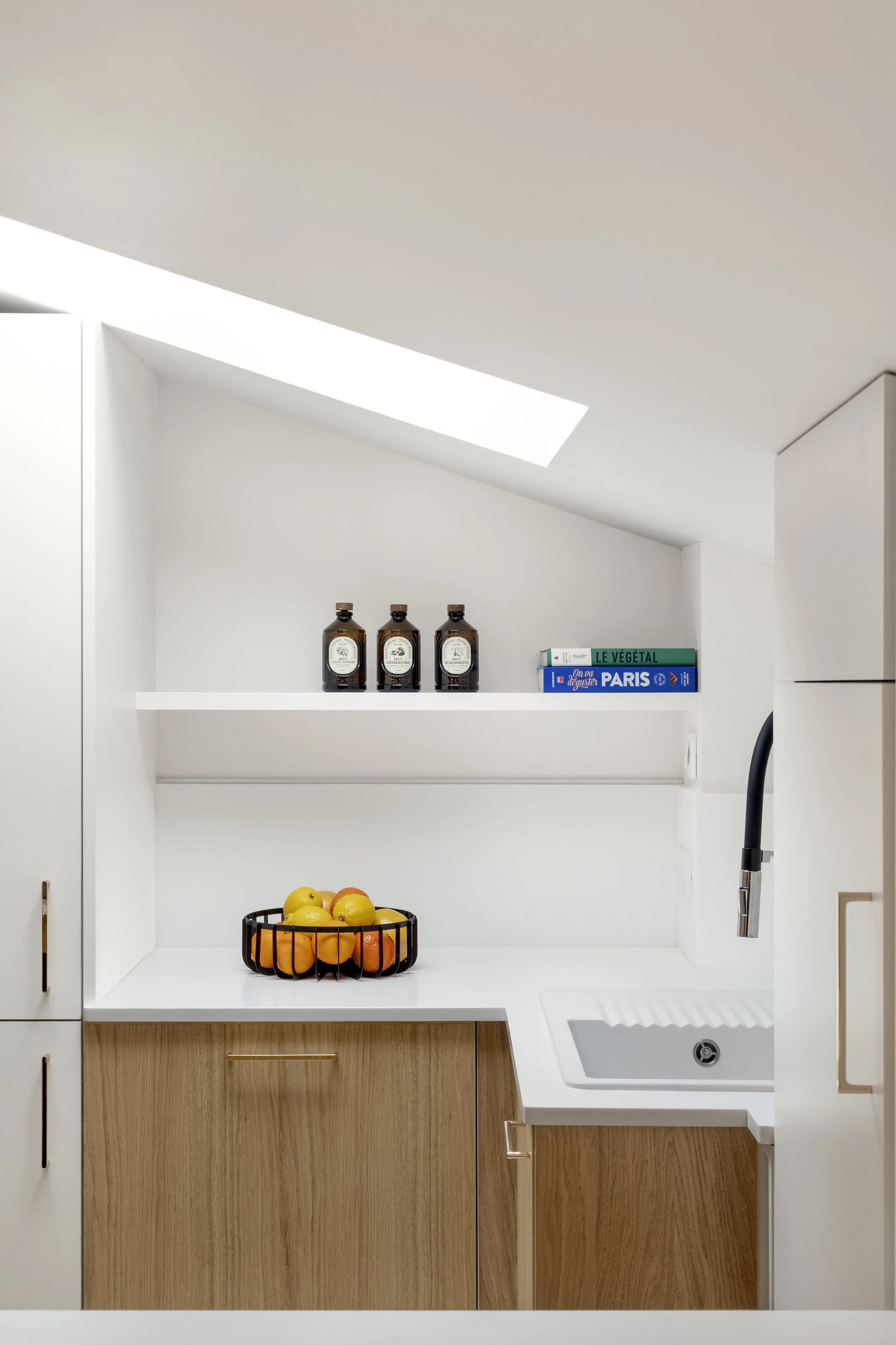cuisine sur mesure sous pente Velux meuble à roulette plan de travail et crédence en résine Corian Krion blanc évier IKEA étagère avec LED poignée de placard La Quincaillerie bois aggloméré mélaminé décor teinte chêne clair panier de fruits livre de 