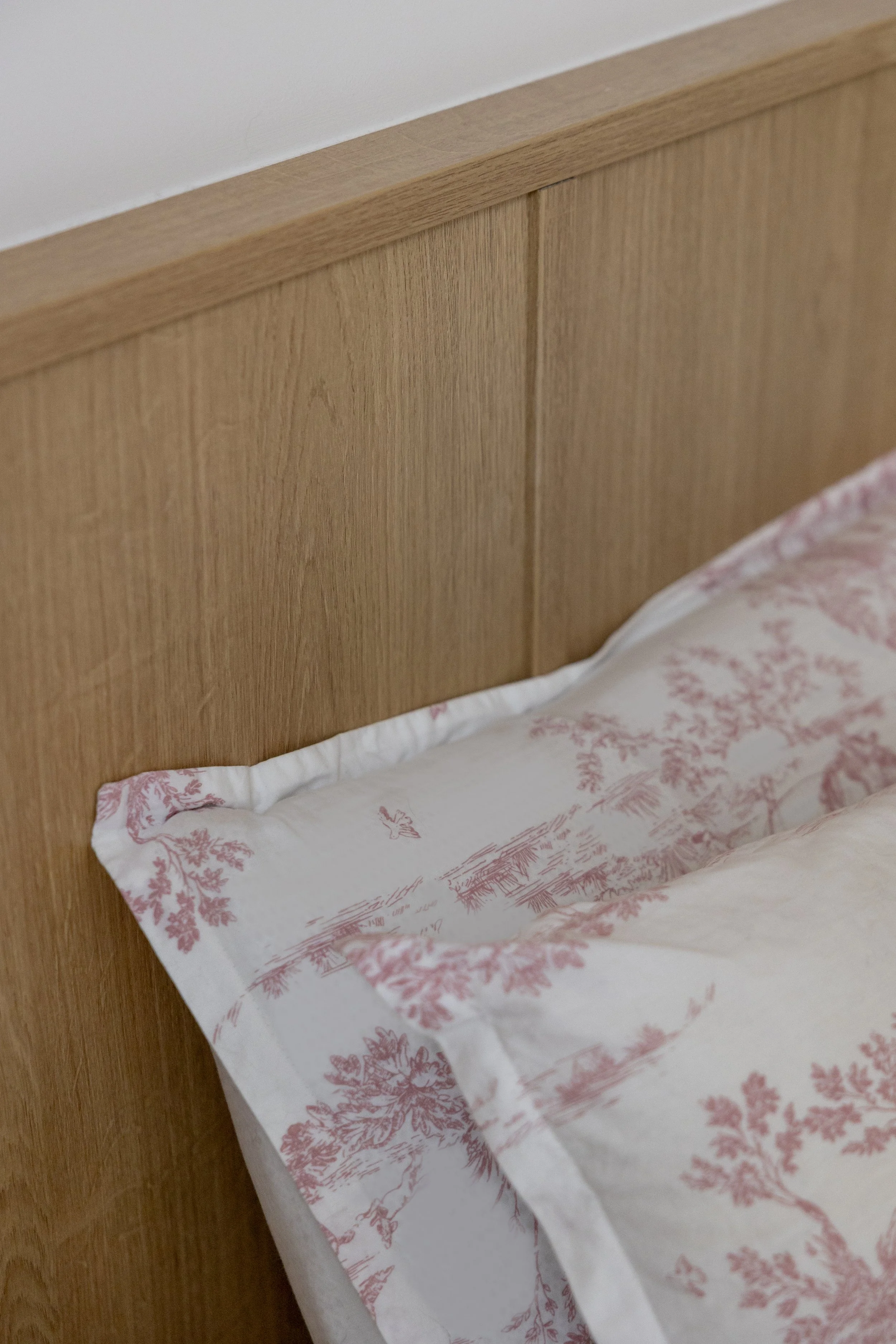 détail constructif tête de lit sur mesure bois aggloméré mélaminé décor bois chêne teinte claire drap blanc et rose oreiller 