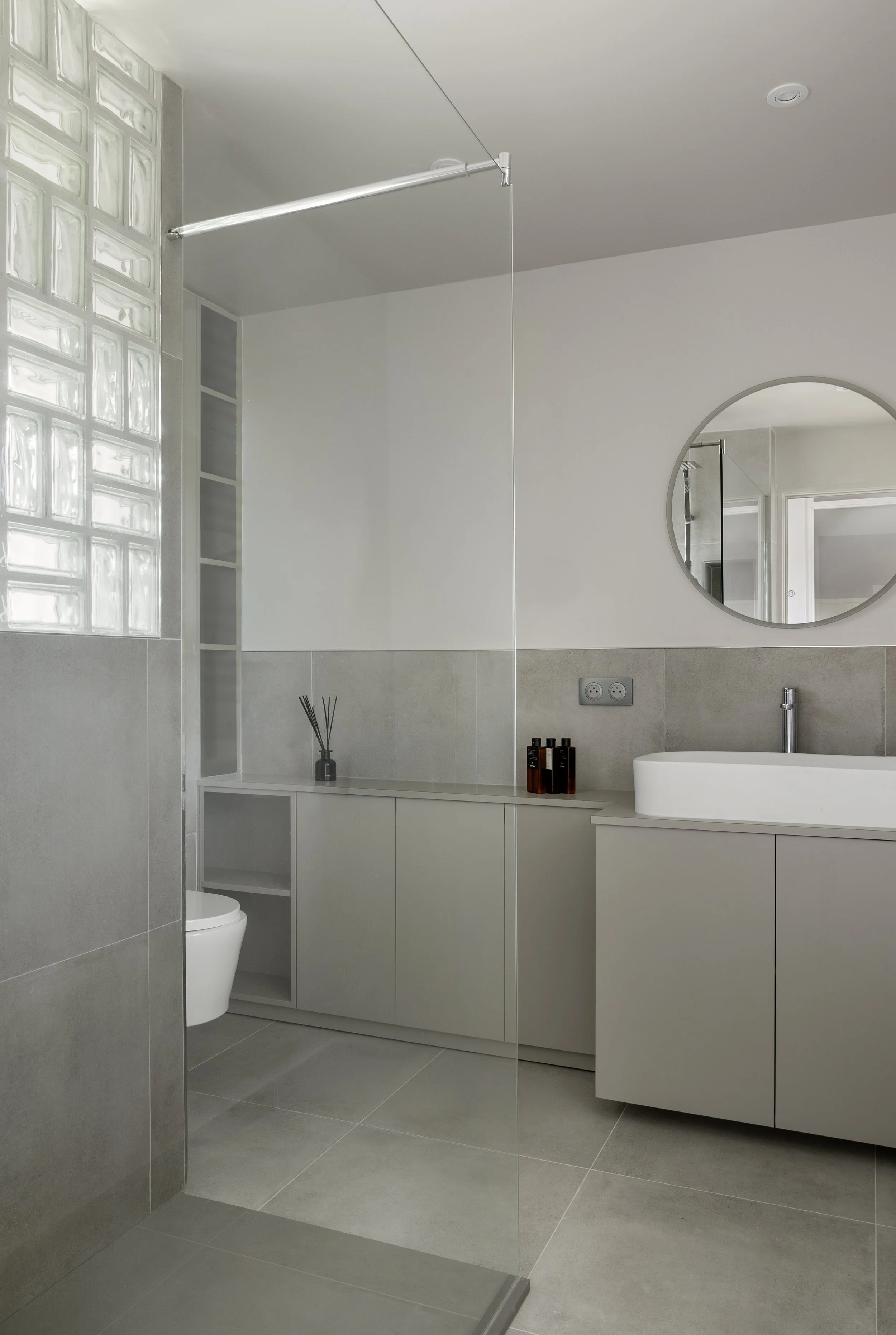salle de bain avec rangement sur mesure placard wc niches carrelage effet béton gris clair vasque à poser rectangulaire en céramique miroir éclairé briques de verres robinetterie hansgrohe paroi de douche en verre interrupteurs Legrand wc suspendu re