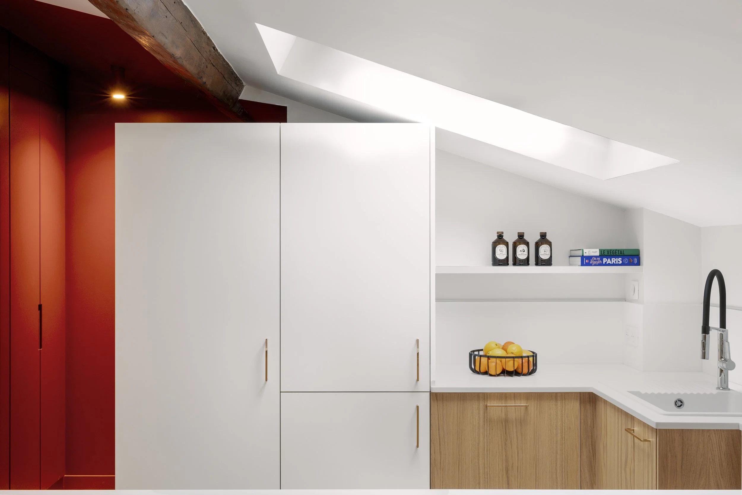 cuisine sur mesure sous pente Velux meuble à roulette plan de travail et crédence en résine Corian Krion blanc évier IKEA étagère avec LED poignée de placard La Quincaillerie bois aggloméré mélaminé décor teinte chêne clair panier de fruits livre de 