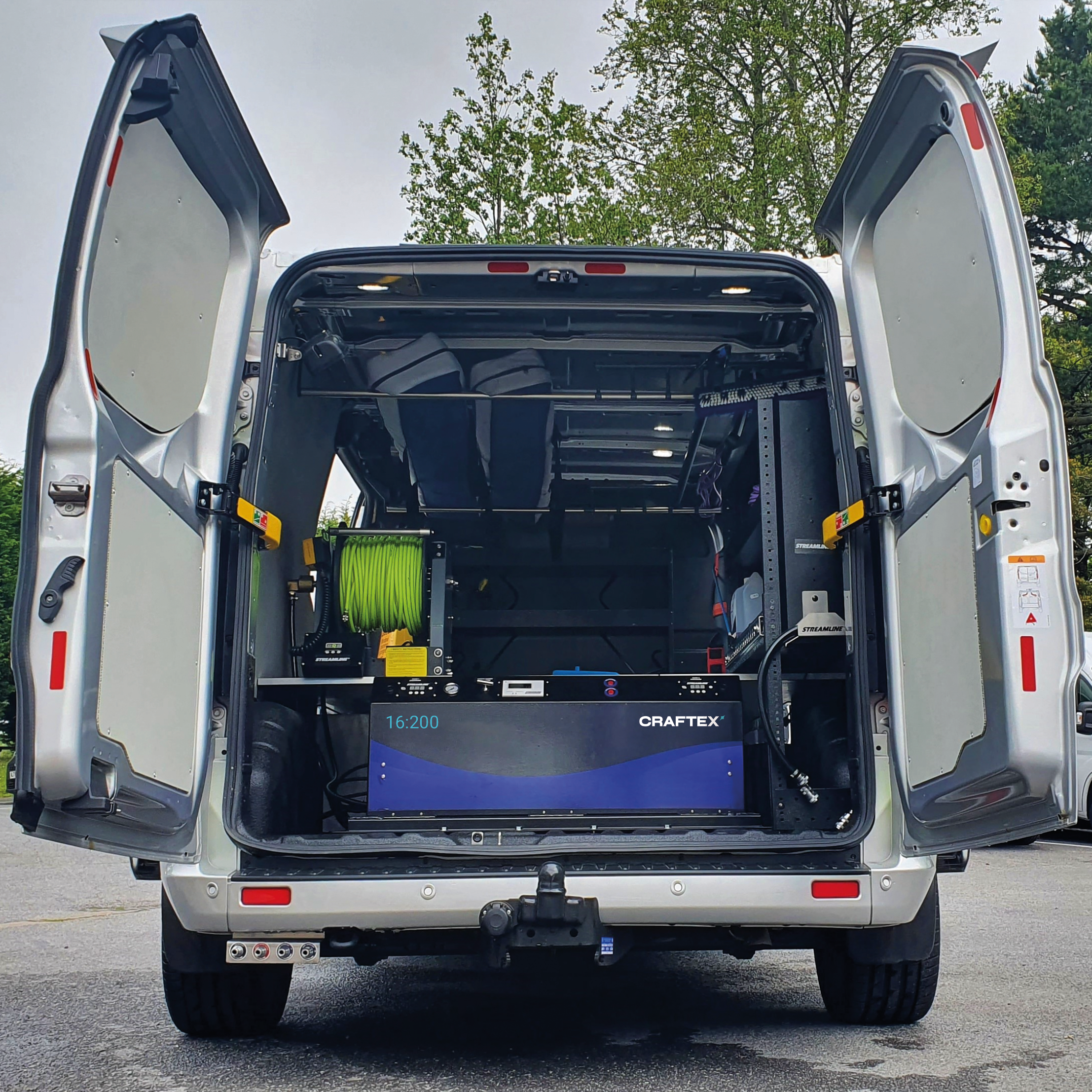 Open rear of a white service van showing a mounted 3D printer, filament spool, and various equipment inside.