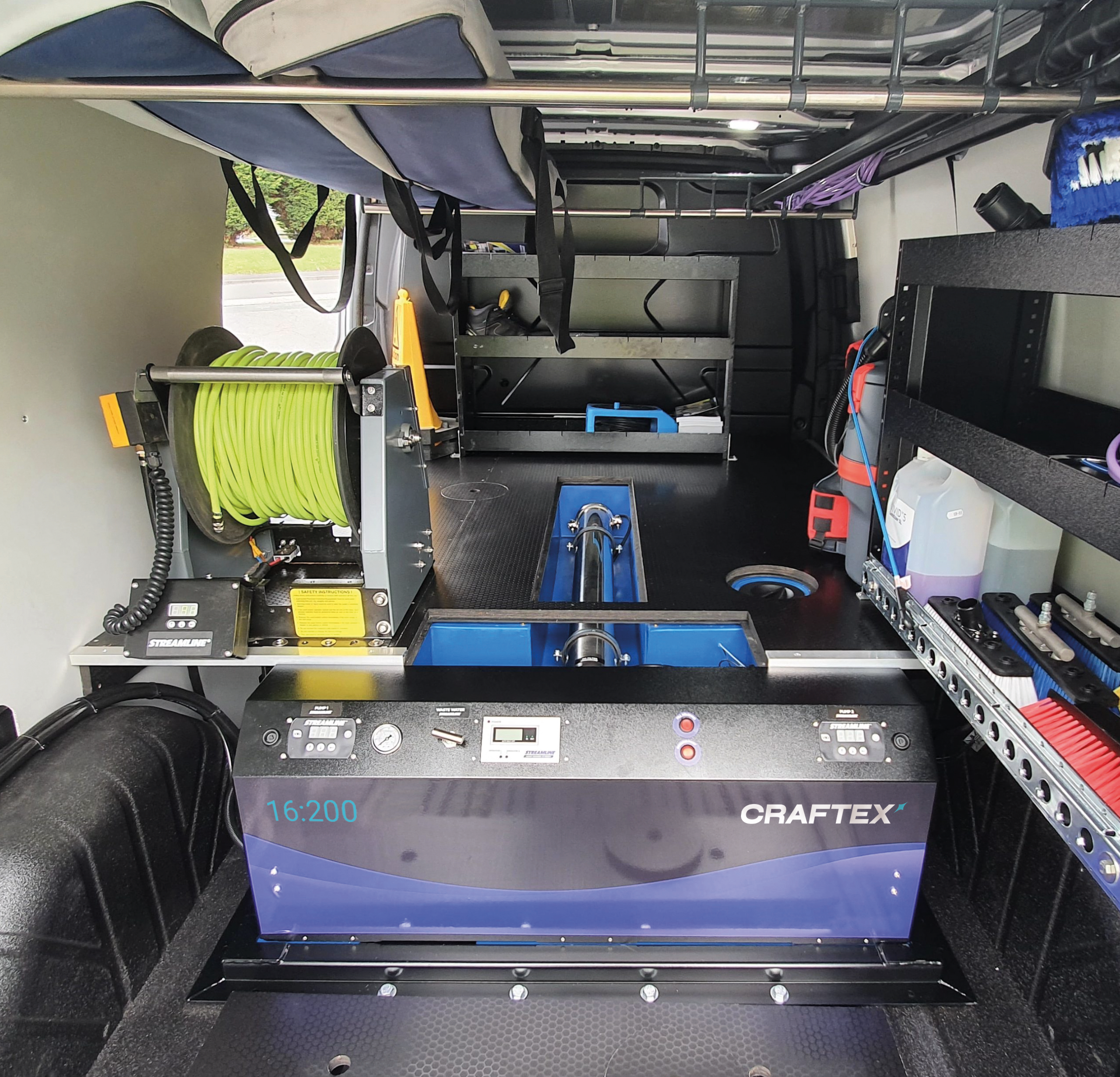 Interior of a service or utility van with equipment including a green hose reel, various tools, and storage shelves.