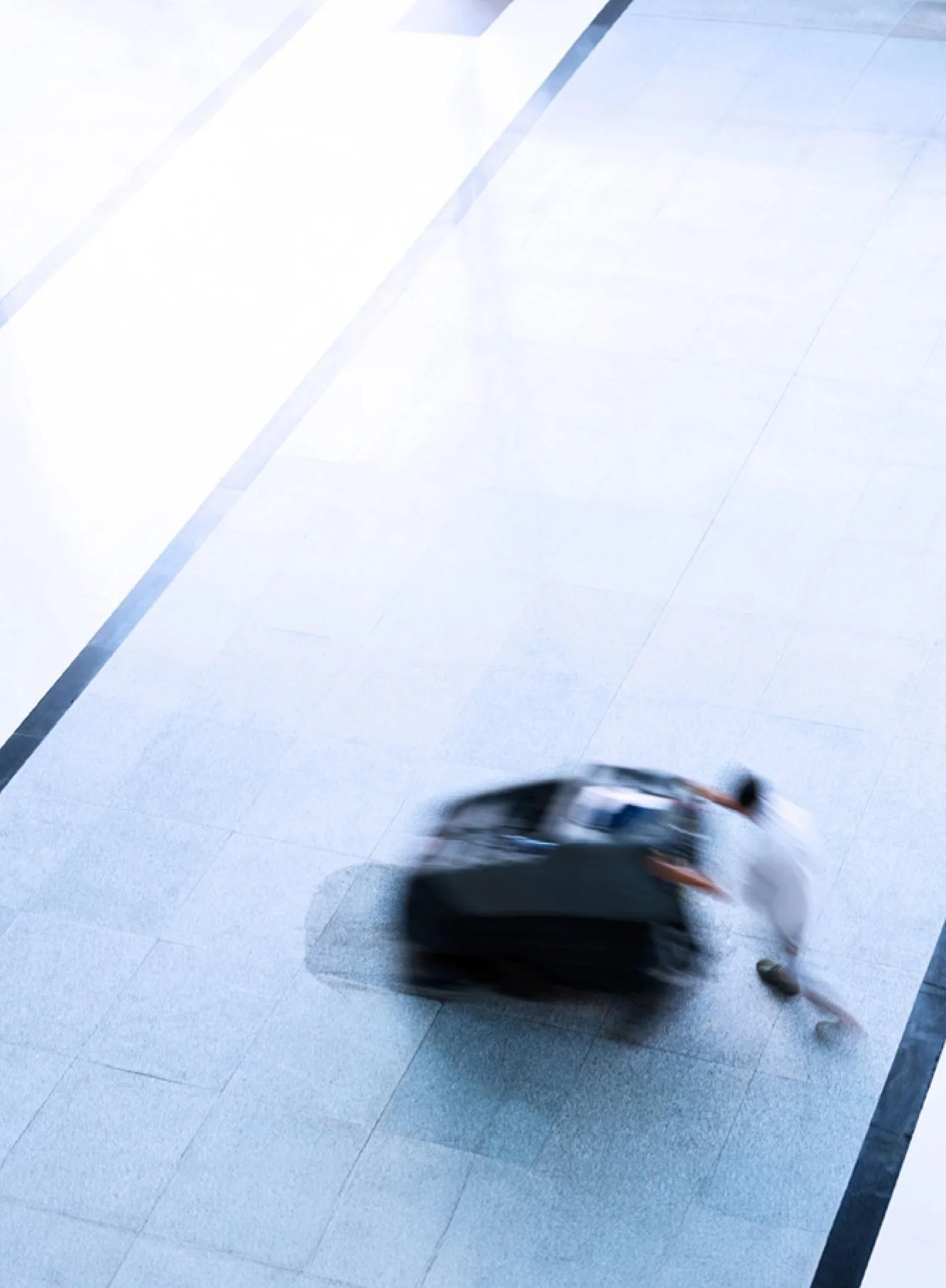 Person with luggage dragging it on the floor in an airport or hotel corridor.