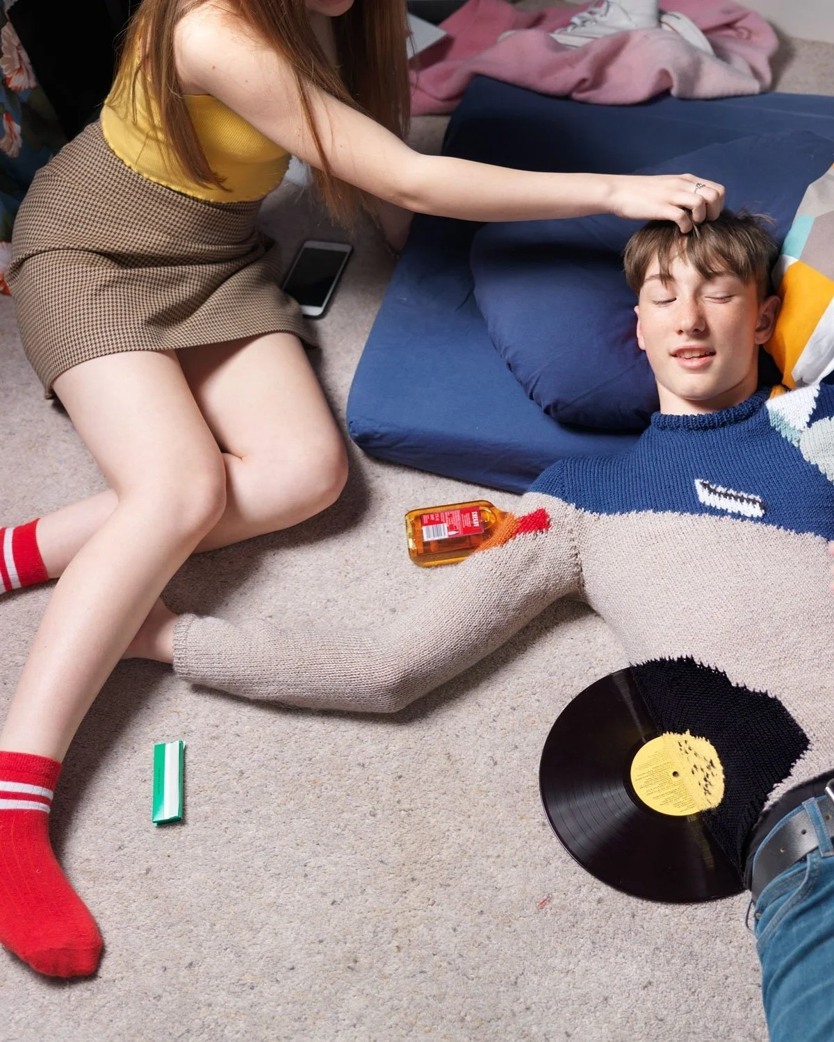 Teen boy in a colour-matching knitted jumper blends into a messy bedroom carpet, surrounded by retro objects, in a surreal optical illusion scene by Joseph Ford