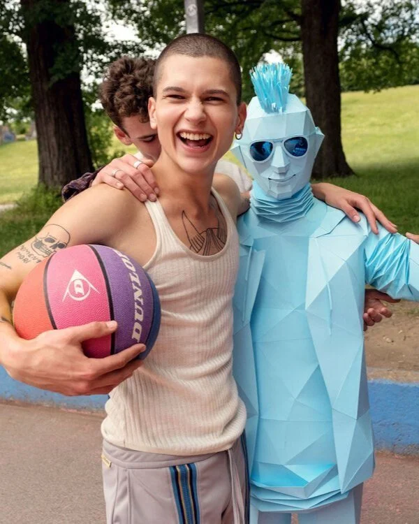 Group of teenagers on a basketball court posing with a geometric blue paper robot figure, photographed by Joseph Ford for a creative youth culture and streetwear-inspired campaign