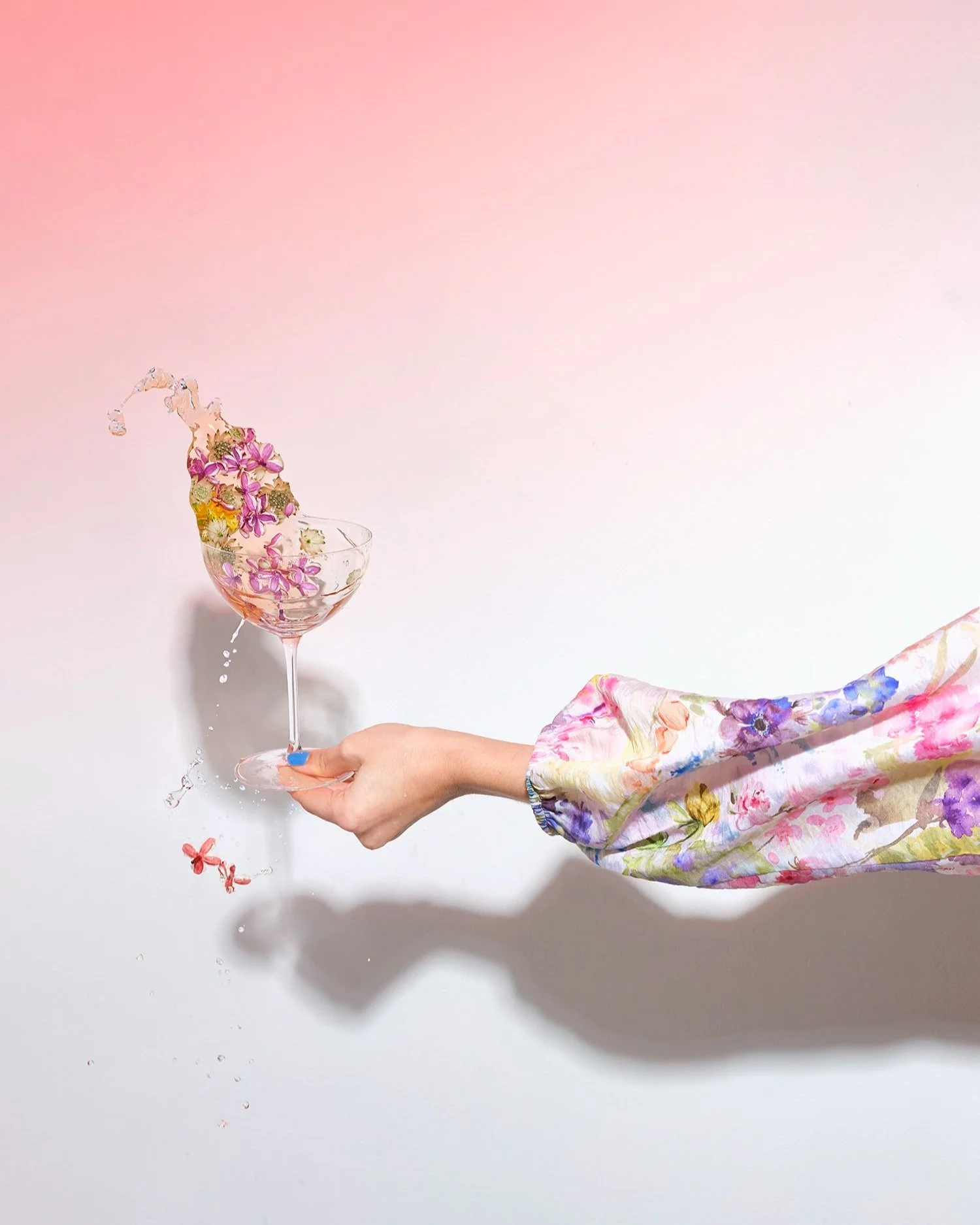 Creative floral cocktail splash by Kellie French for The Observer – a hand in a floral sleeve holding a coupe glass as water and spring flowers dramatically spill mid-air 