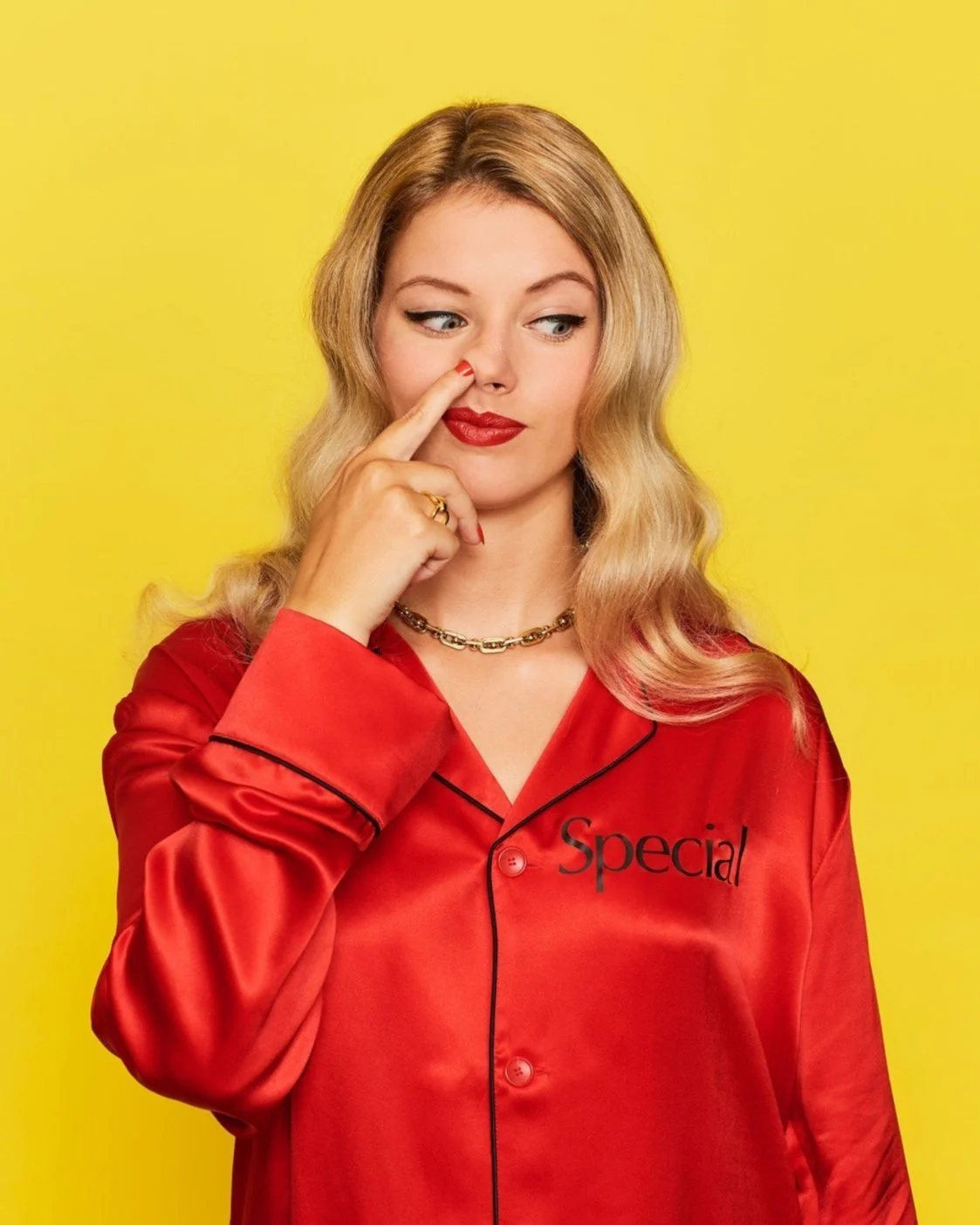 Humorous editorial portrait by Kellie French for The Guardian, showing a woman in glossy red pyjamas with 'Special' embroidered on the chest, playfully picking her nose 