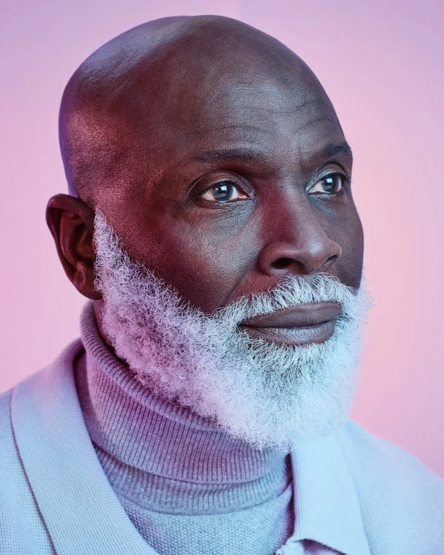 Close-up of mature man with white beard in lilac roll-neck, photographed by Phil Fisk for Vyxeos campaign, against pink-purple gradient background