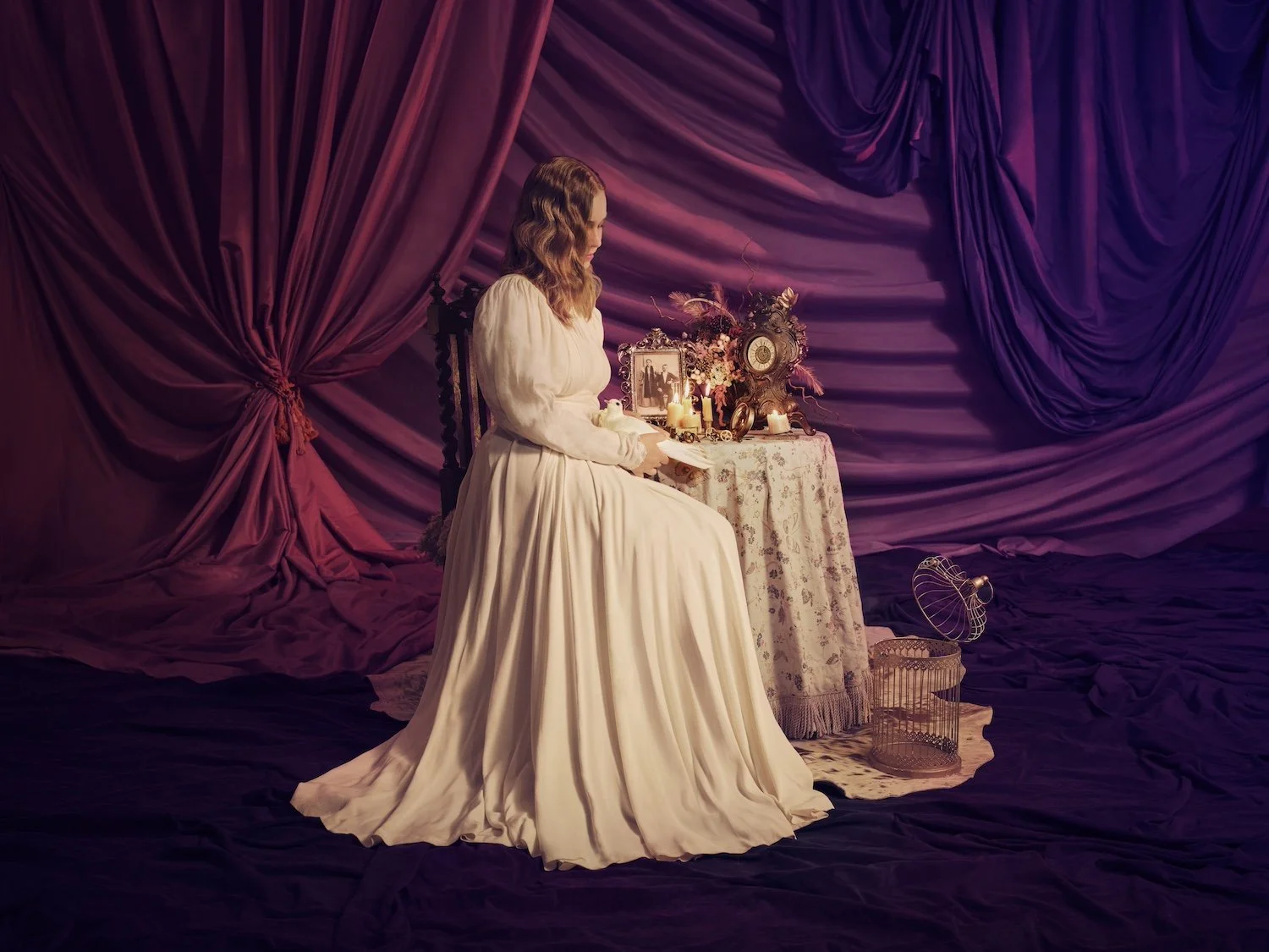 Conceptual portrait of a woman in flowing gown seated at vintage vanity surrounded by candles and personal relics for Three Sisters at Shakespeare Globe, art-directed by Phil Fisk