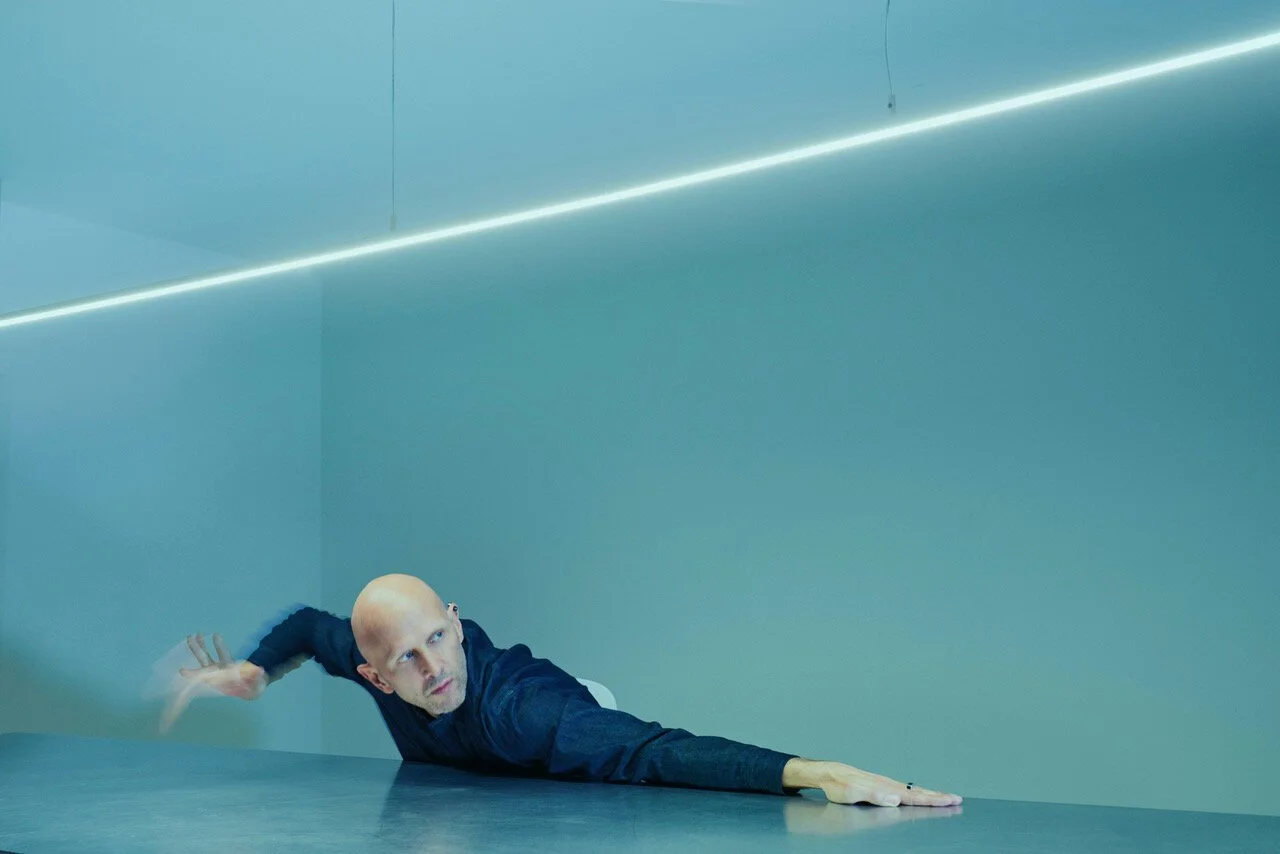 Stylised portrait of performer Jonathan McGregor in dynamic pose under architectural lighting, photographed by Phil Fisk, London photographer. Conceptual editorial photography with minimalist blue tones.