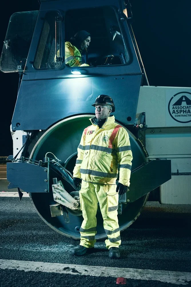 Nighttime portrait of road workers beside a steamroller, photographed by Phil Fisk 