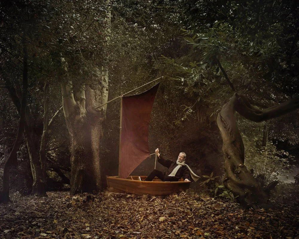 Surreal portrait of Terry Gilliam in a small wooden boat among twisted trees, photographed by Phil Fisk for a BAFTA project. Editorial image with storybook lighting and whimsical forest setting, shot in London.