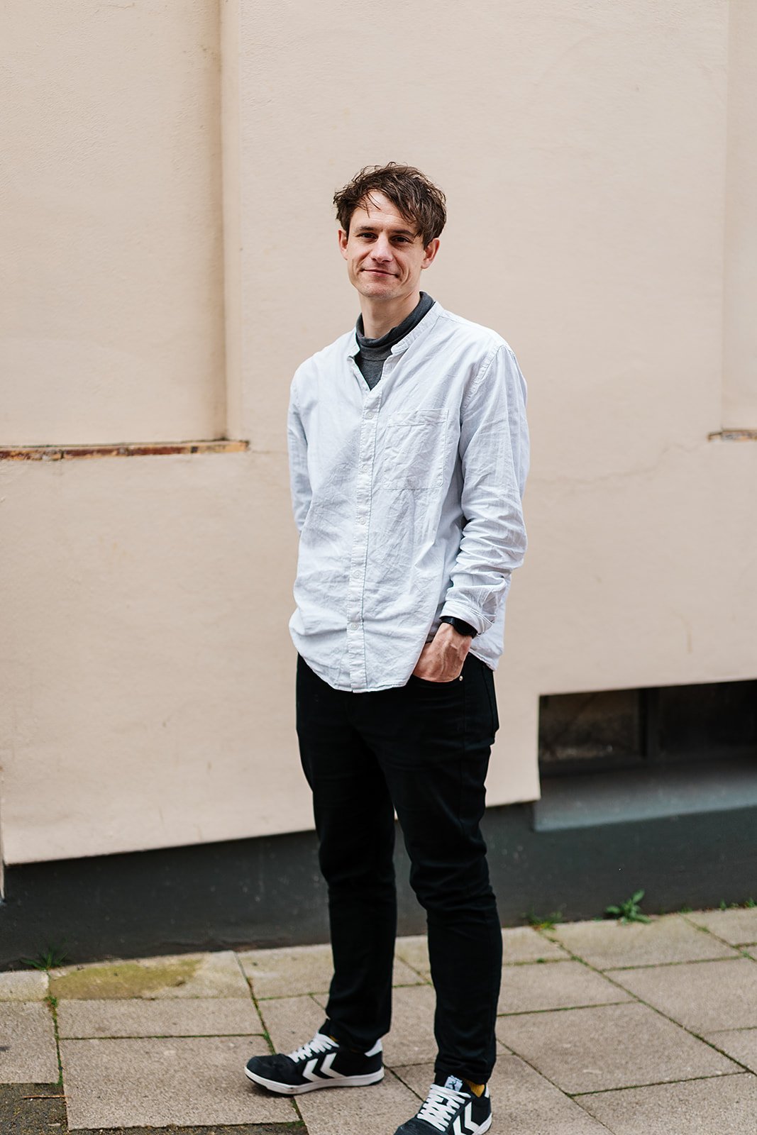 Man in white shirt and black pants stands outdoors on a sidewalk.