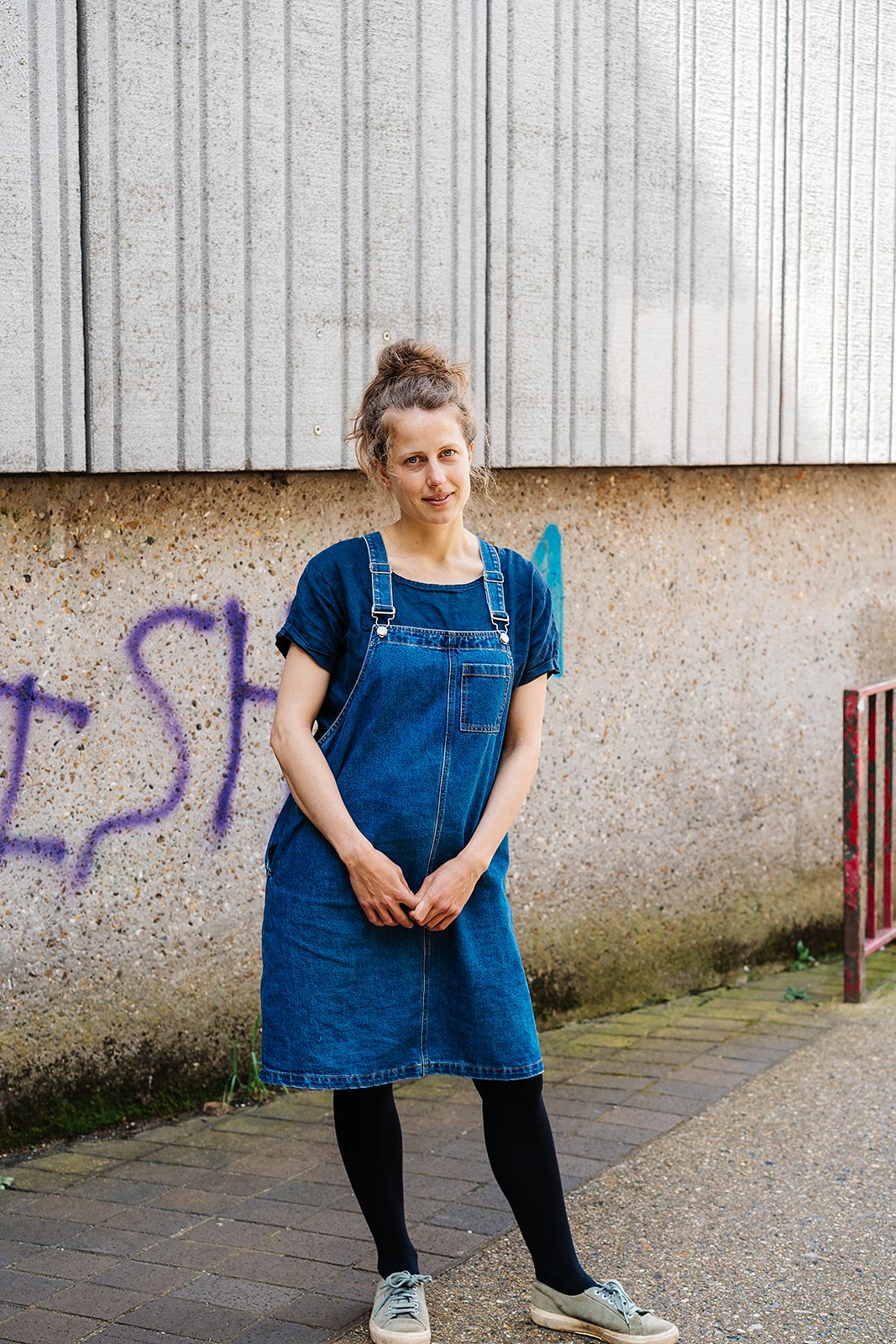 Person in denim dress standing against graffiti wall