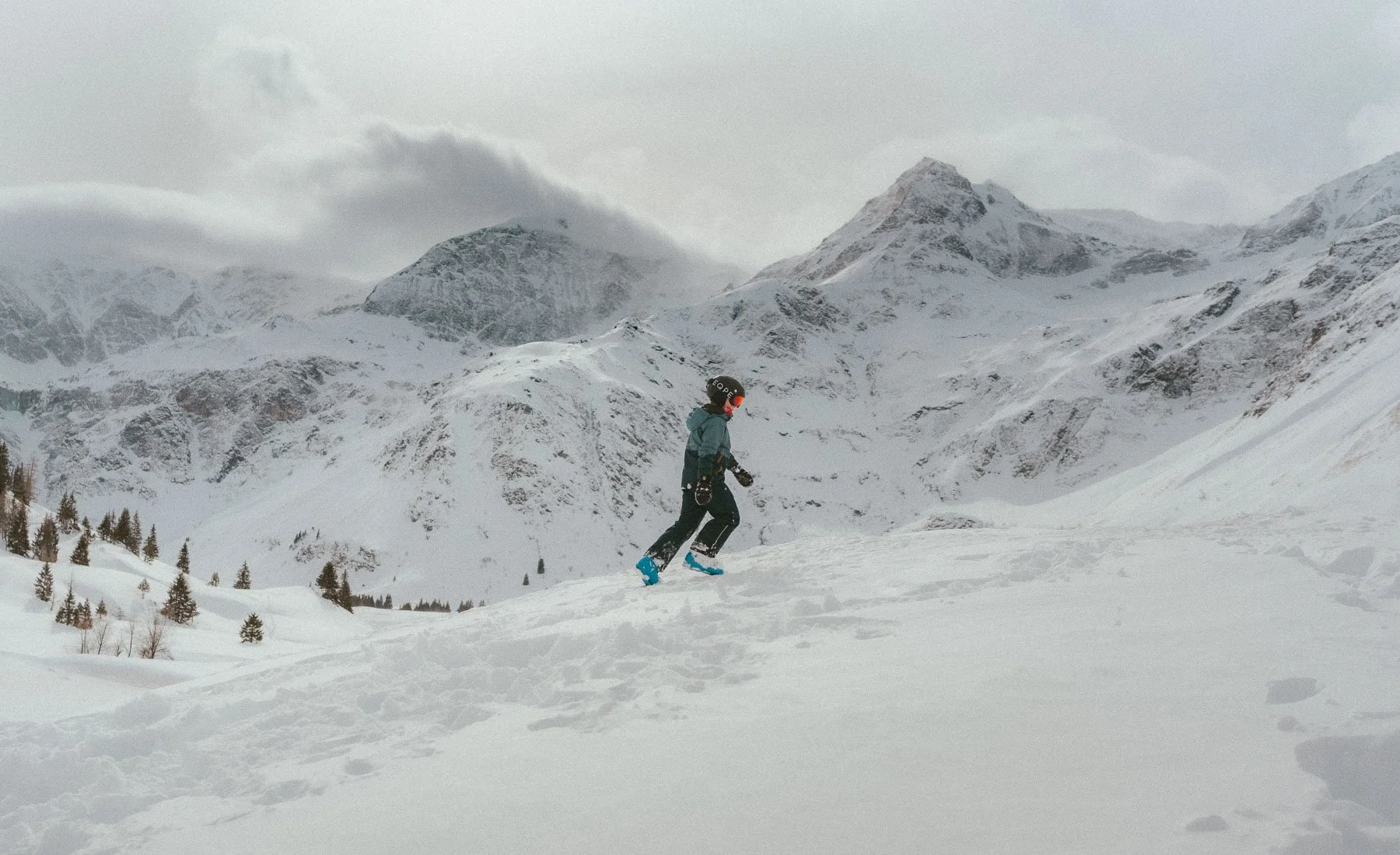 Persoon in skibroek, jas en helm die door een besneeuwd berglandschap skiet.
