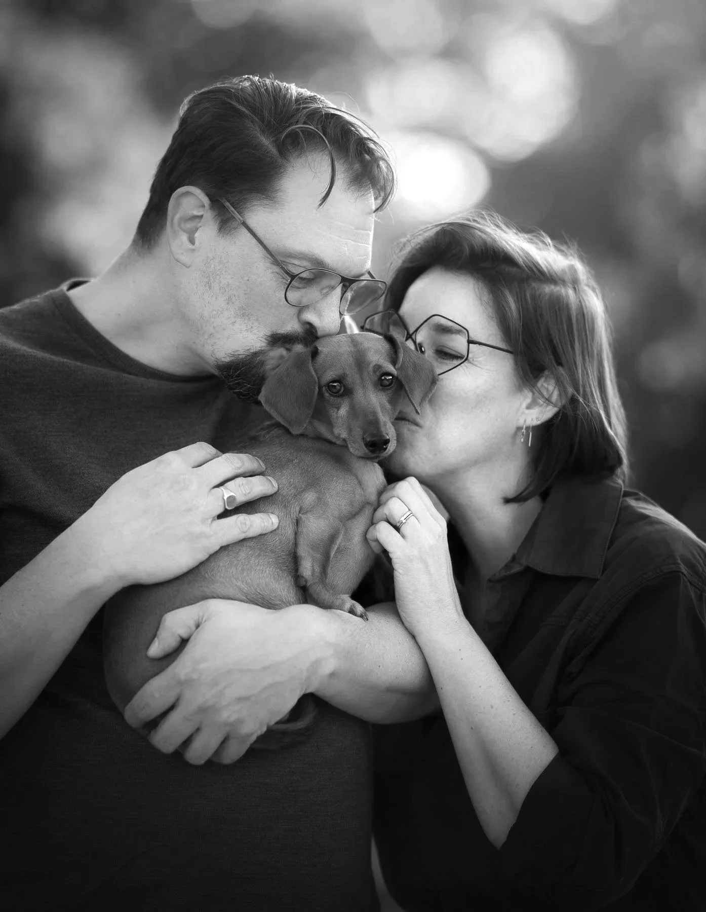 Twee mensen en een hond omhelzen elkaar liefdevol, zwart-wit foto.