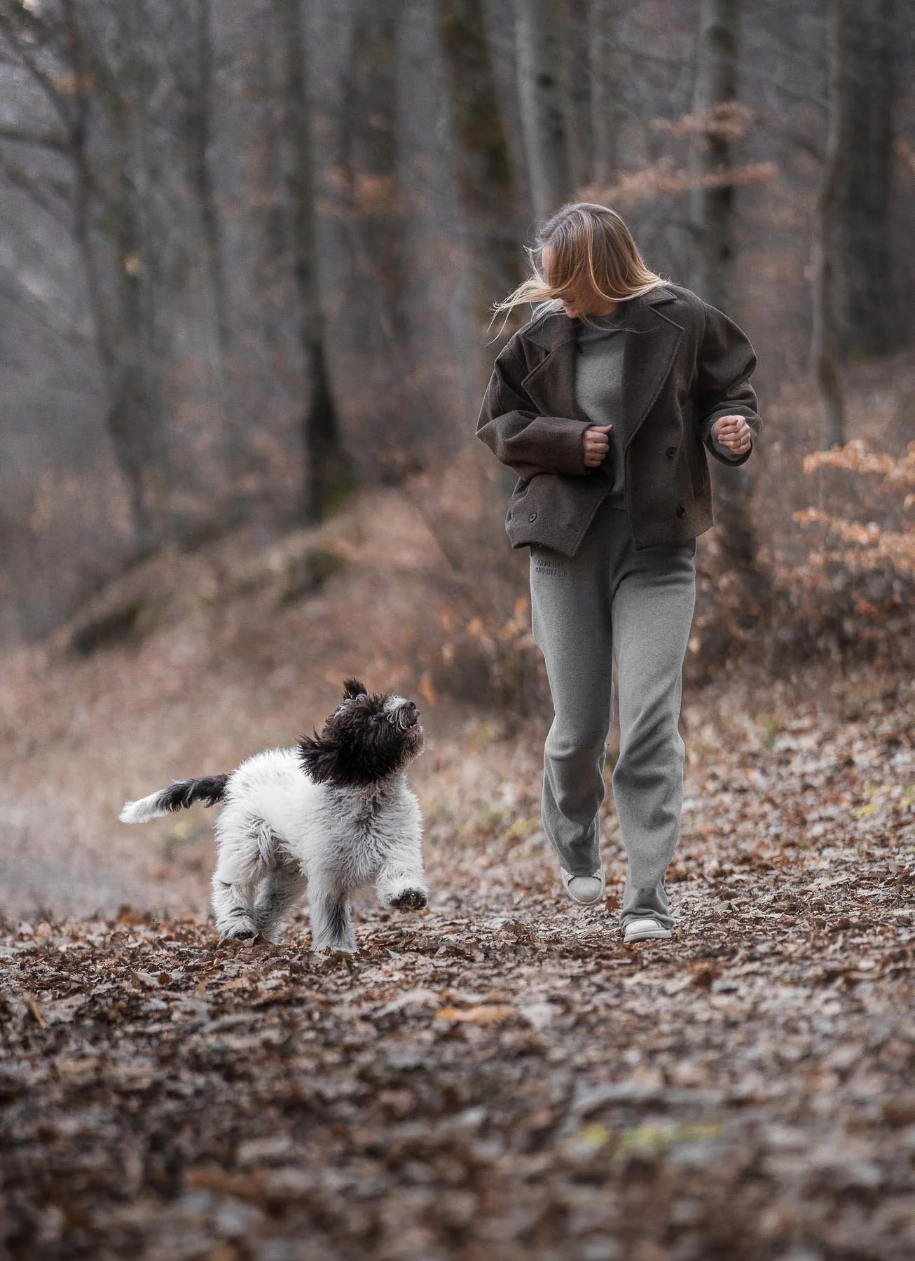 Vrouw wandelt met haar hond in een bos in de herfst, beide lijken te genieten van een frisse wandeling.