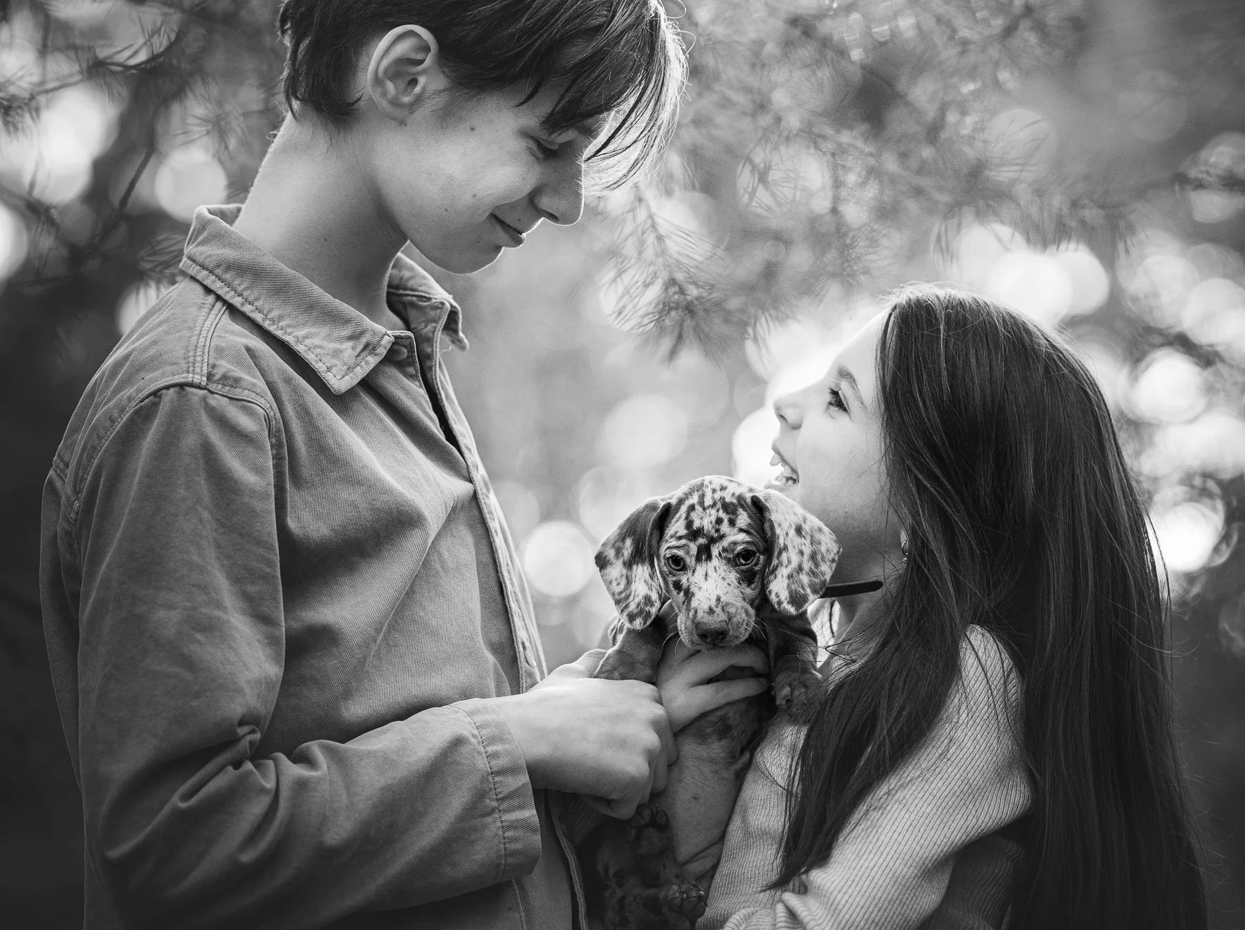 Een zwart-wit foto van twee vrouwen die naar elkaar kijken terwijl ze een puppy vasthouden. De achtergrond is wazig met bokeh-effecten.