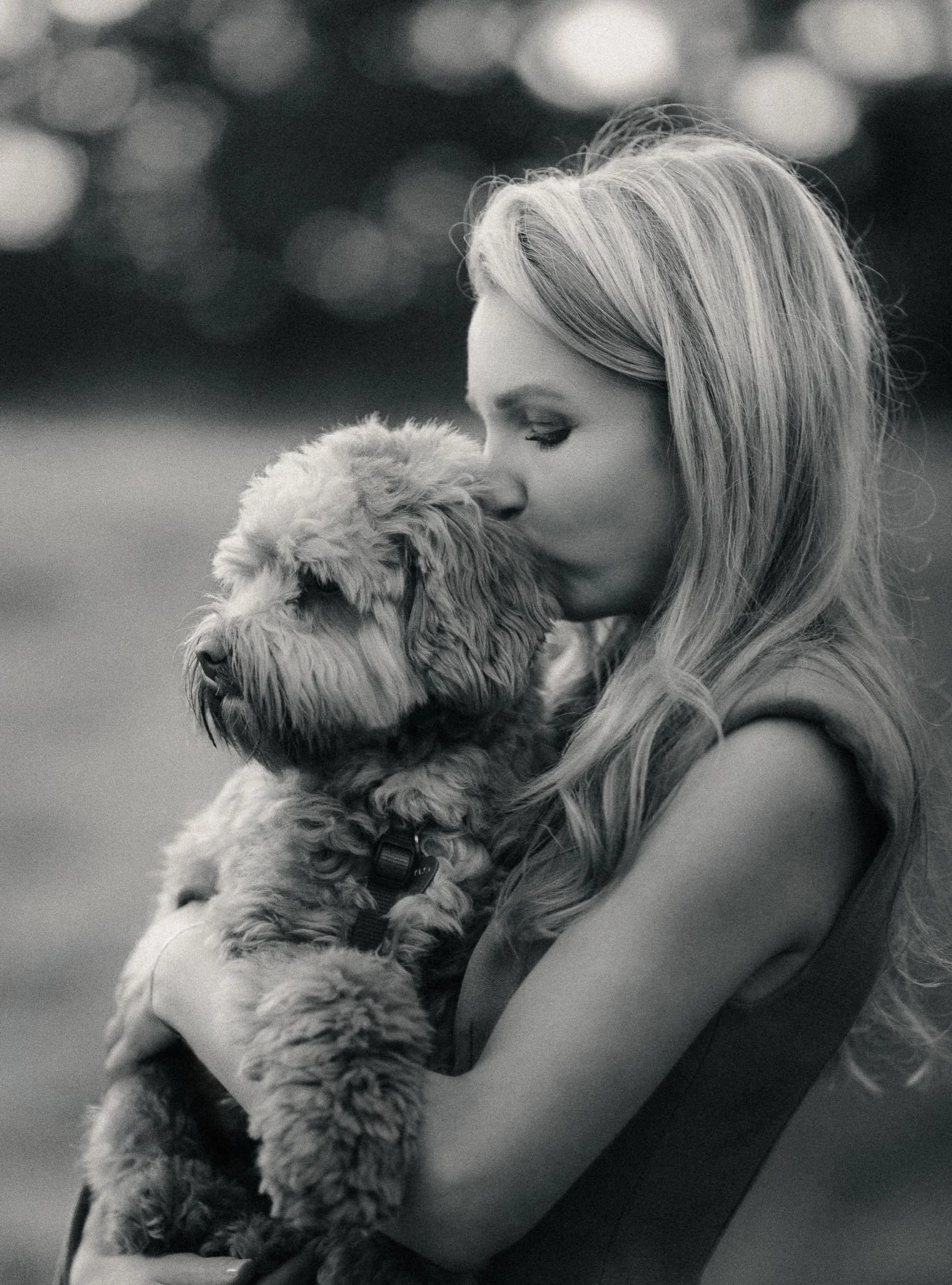 Een vrouw met lang, golvend haar houdt een schattige, pluizige puppy dicht tegen haar gezicht, beiden lijken te genieten van een tedere moment.