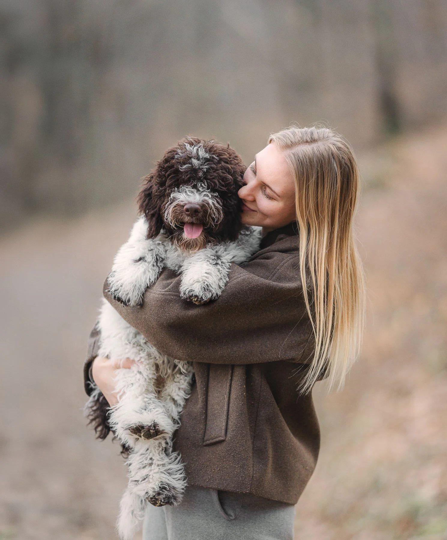 Een vrouw houdt haar hond liefdevol vast tijdens een ontspannen moment in de natuur. De foto straalt rust, verbondenheid en de band tussen mens en hond uit.