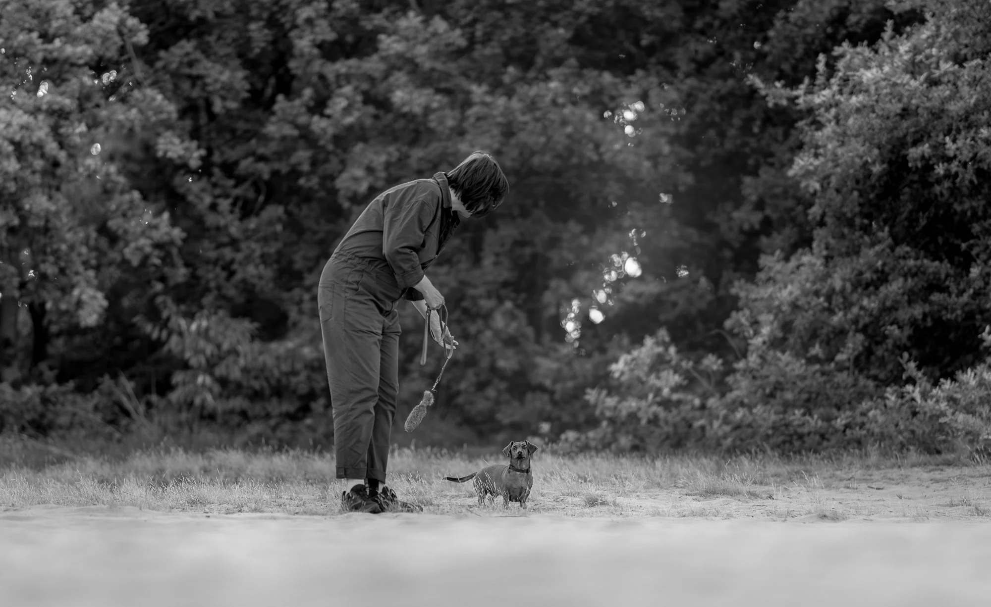 Artistieke zwart-wit hondenfotografie van teckel en twee eigenaren tijdens fotoshoot in de natuur.
