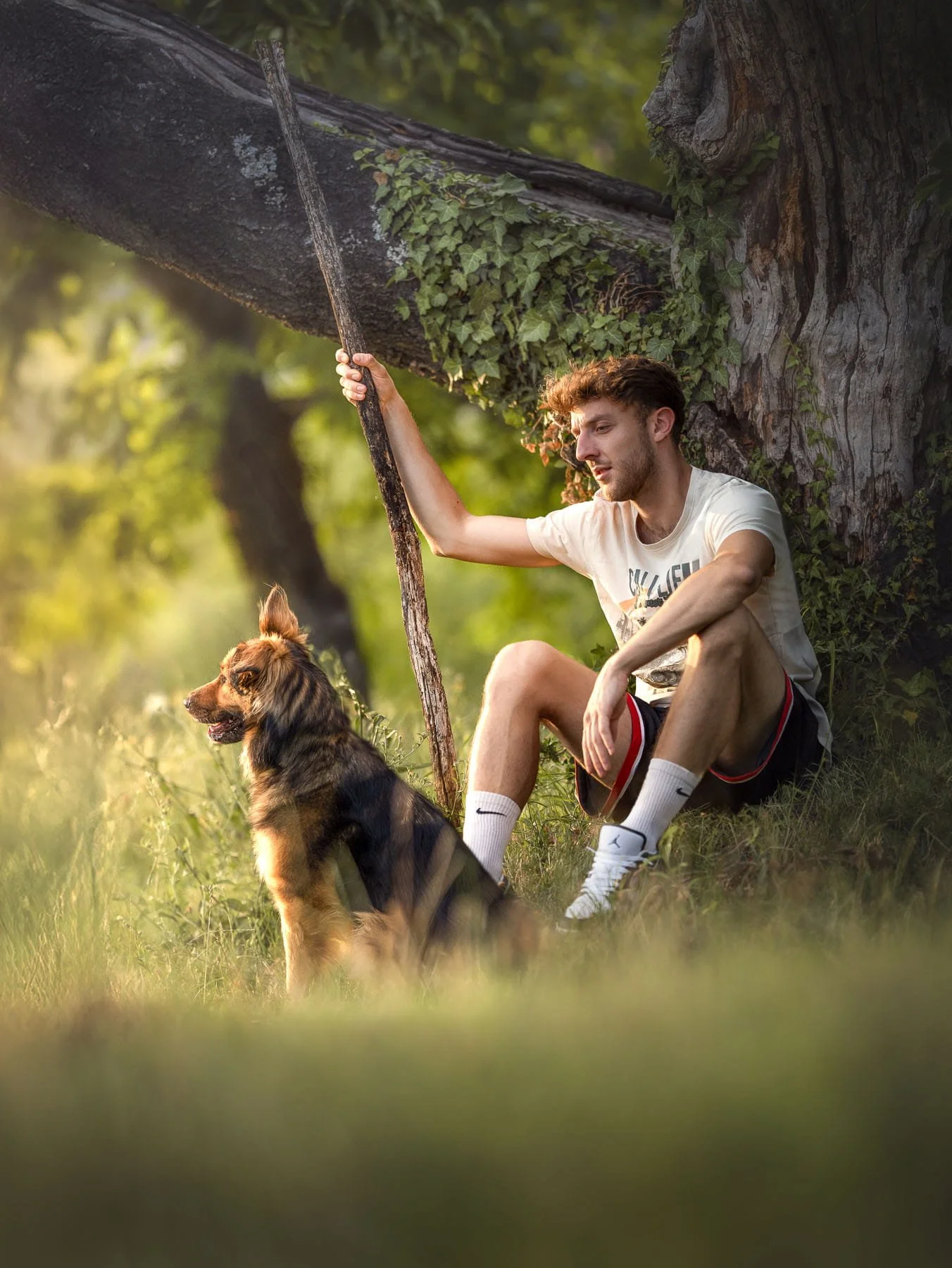 Jongen zit onder een boom met zijn hond in een bosrijke omgeving.