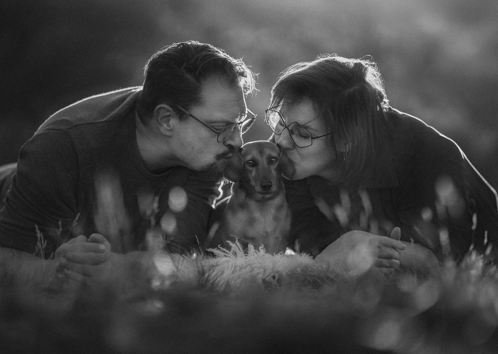 Minimalistisch zwart-wit portret van teckel in de duinen samen met twee eigenaren