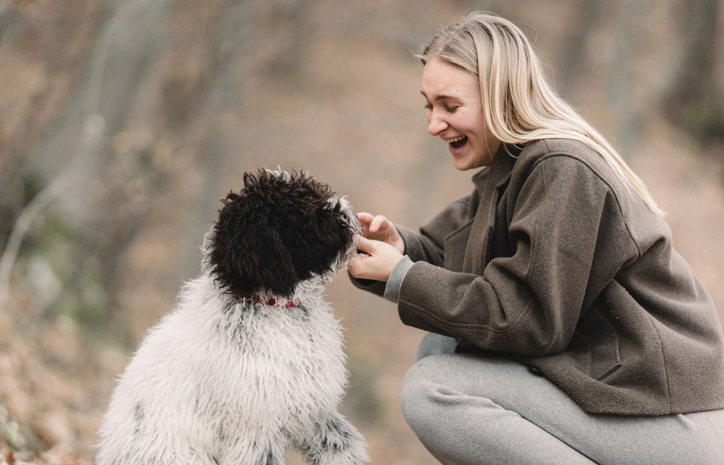 vrouw met blond haar speelt met zwart witte krulhond in natuurlijke omgeving buiten