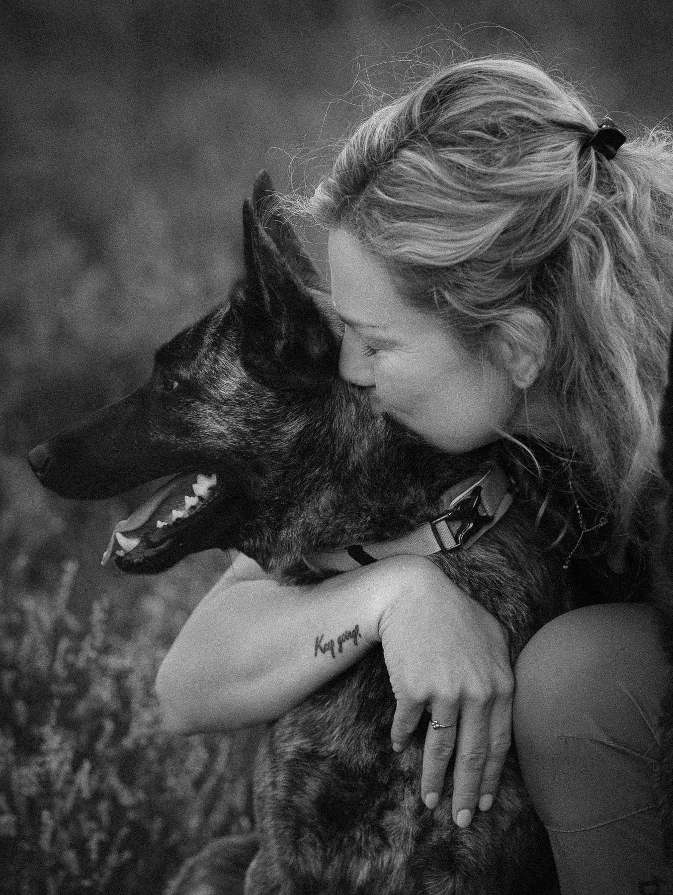 Een vrouw die haar hond omhelst en kusjes geeft. De foto is zwart-wit.