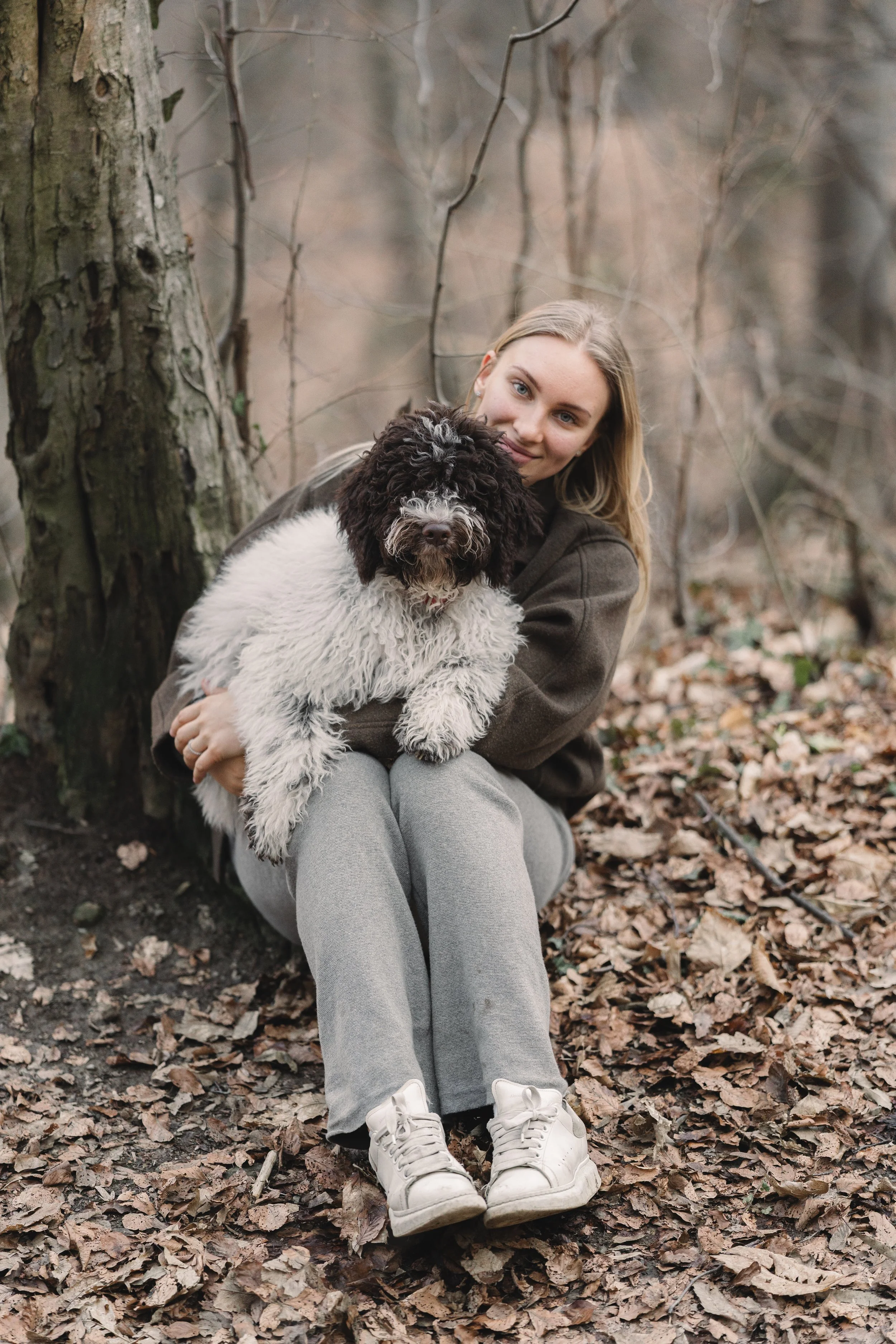 portret van vrouw met hond in bos met bladeren op de grond en natuurlijke achtergrond