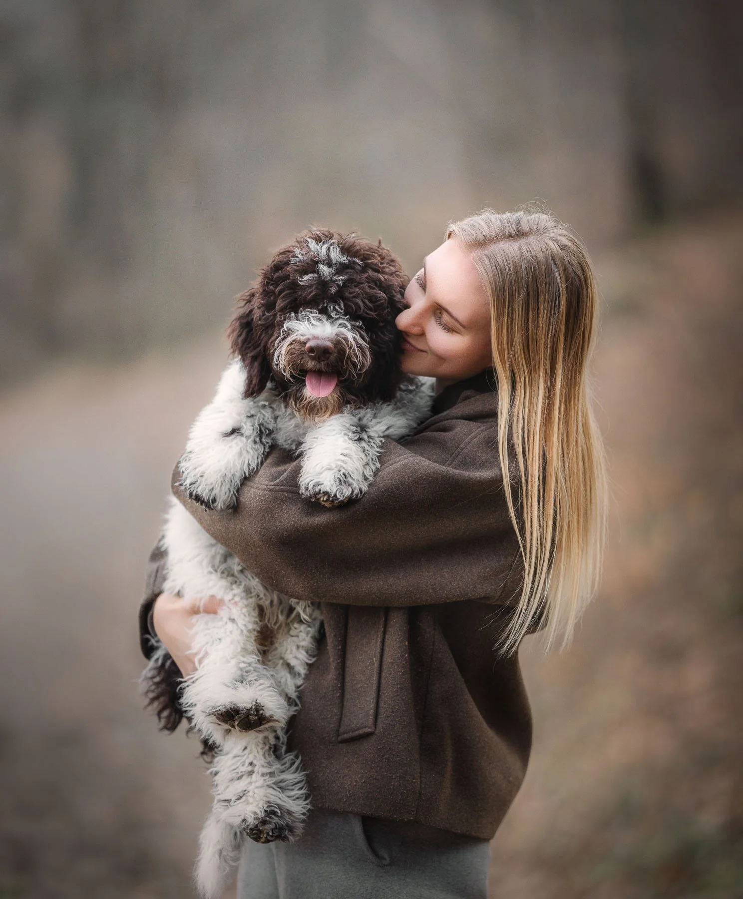 Vrouw die een schattige, gekrulde hond vasthoudt en knuffelt, buiten in een natuurlijke omgeving.