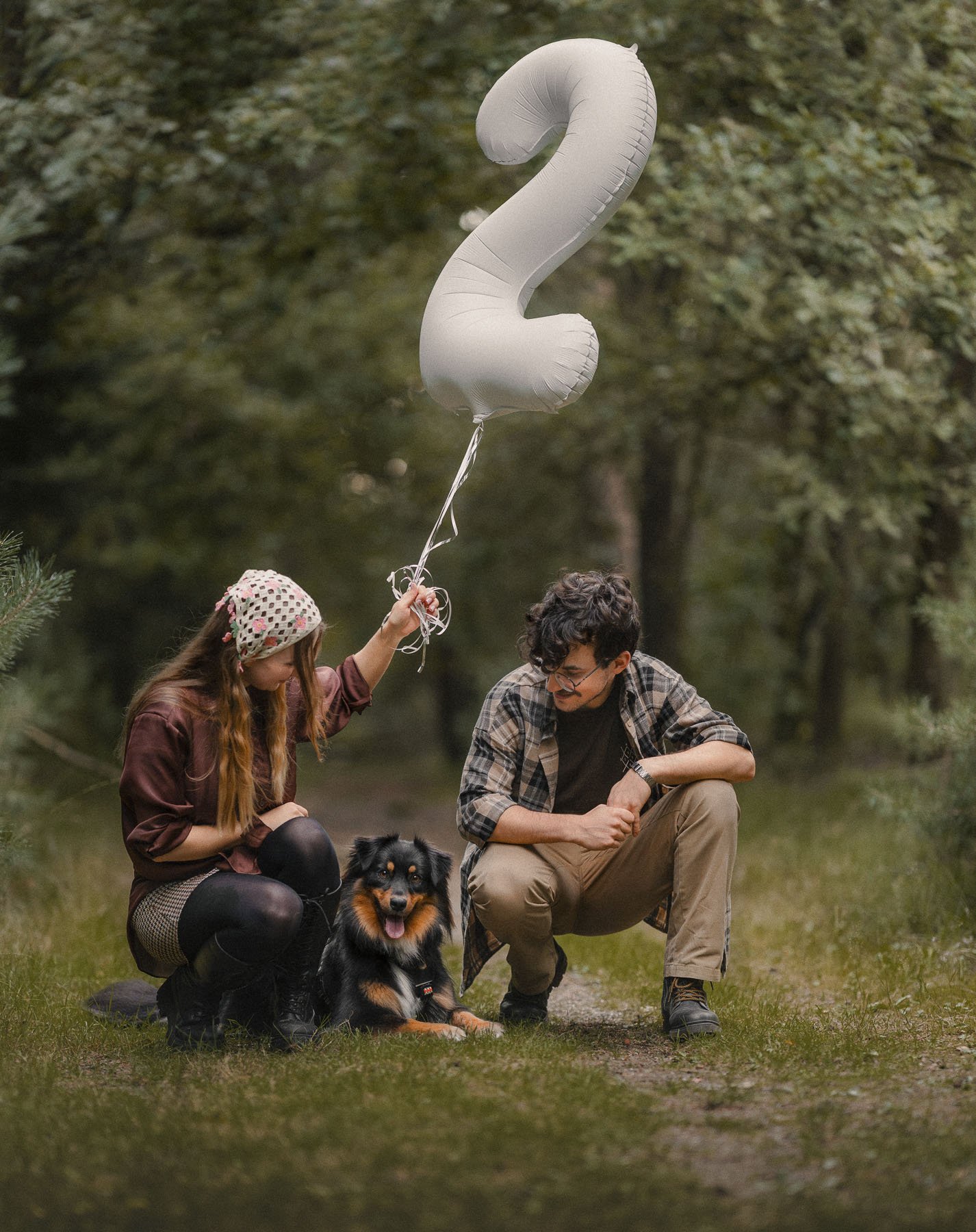 Twee mensen en een hond in een bos, met een witte ballon in de vorm van een vraagteken.
